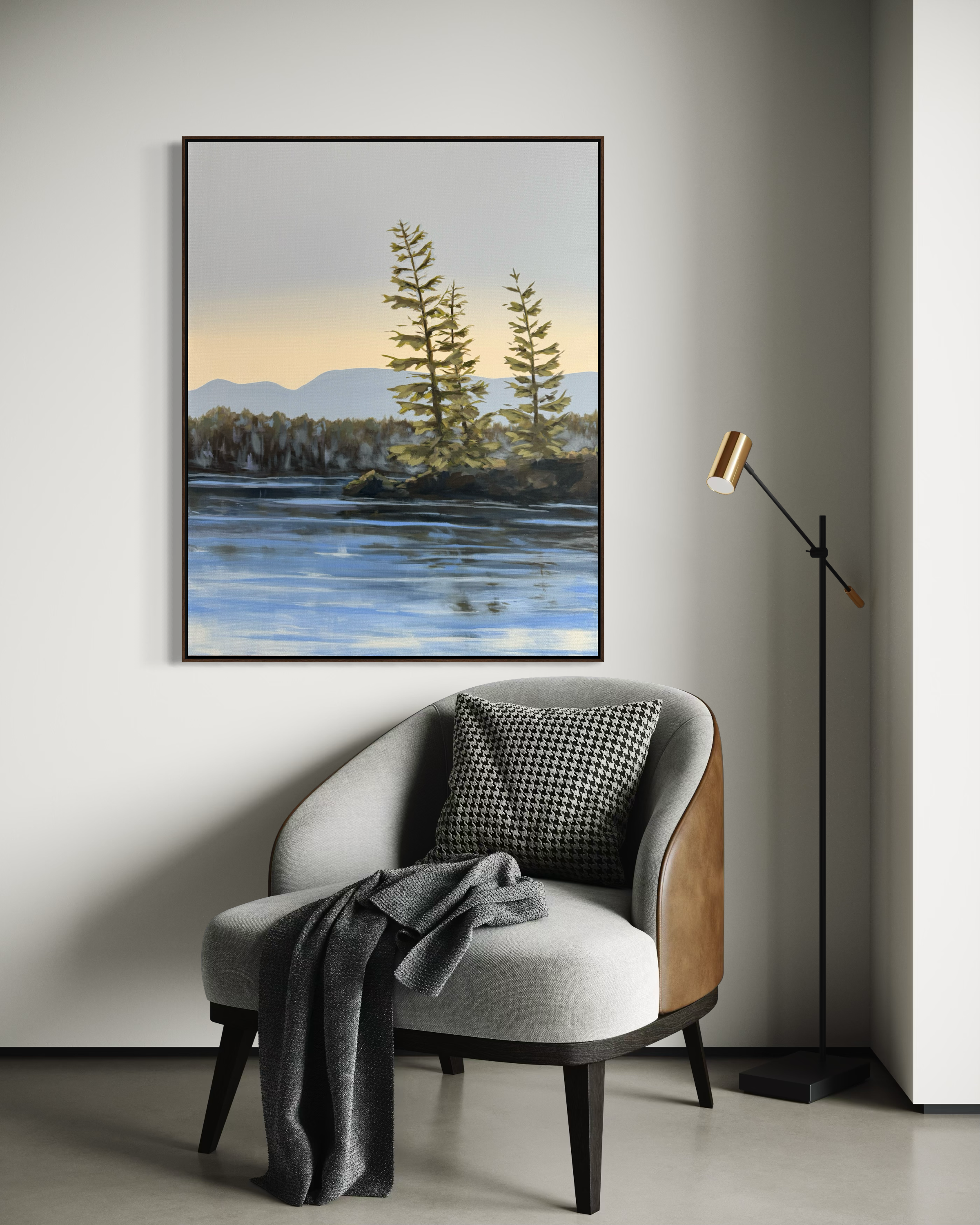 A cozy living room corner with a modern armchair, a black and white throw pillow, a dark gray blanket, a floor lamp with a gold and black design, and a large landscape painting of trees and water on the wall.