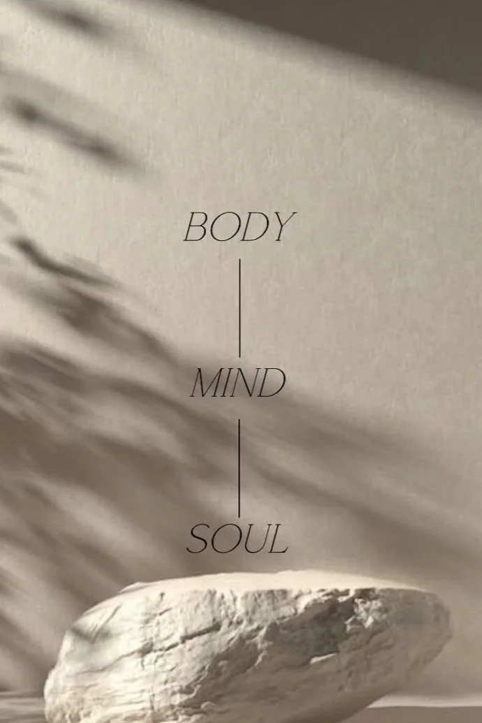 Inspirational quote with a white stone on a neutral background. The quote reads, 'Body, Mind, Soul' divided by lines.