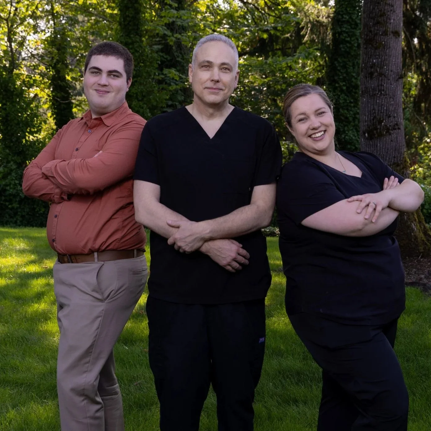 The Chiropractic of Bellevue team, standing outdoors on a grassy area with trees in the background, smiling and crossing their arms.