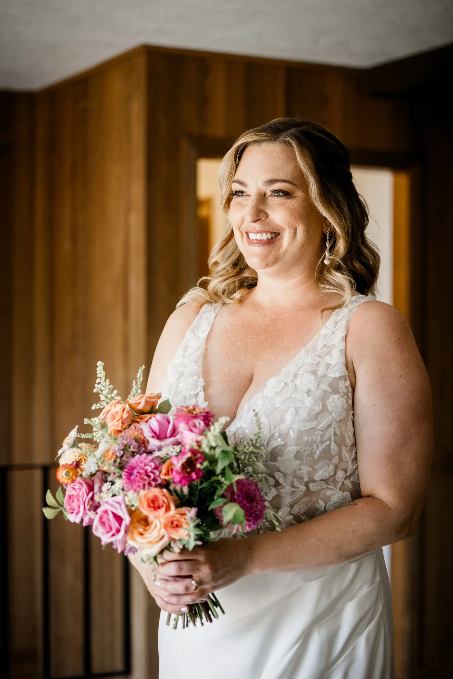 A woman in a white wedding dress holding a bouquet of pink and peach flowers, smiling