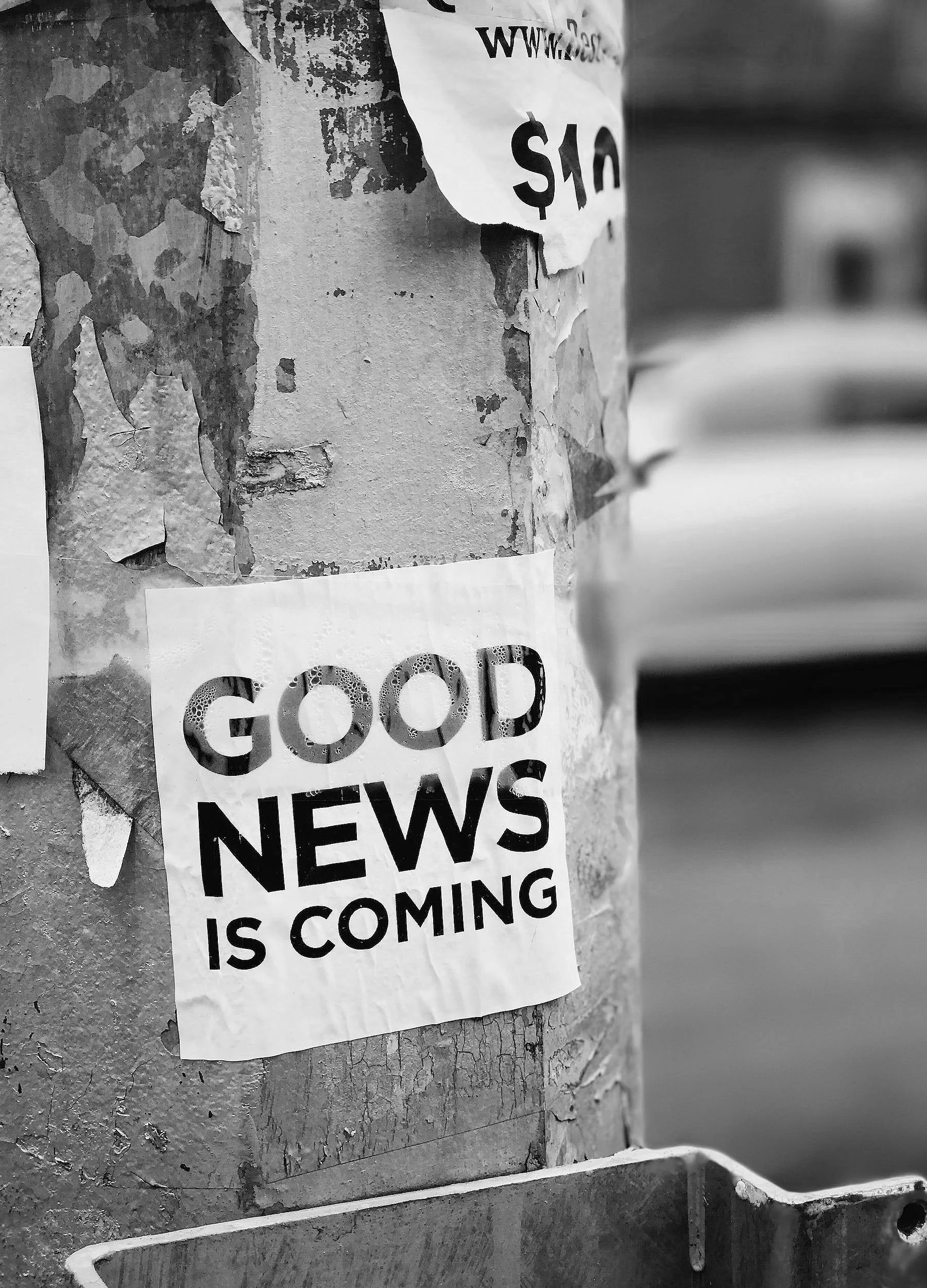 A poster on a weathered wall with peeling paint reads, 'GOOD NEWS IS COMING' in large letters.