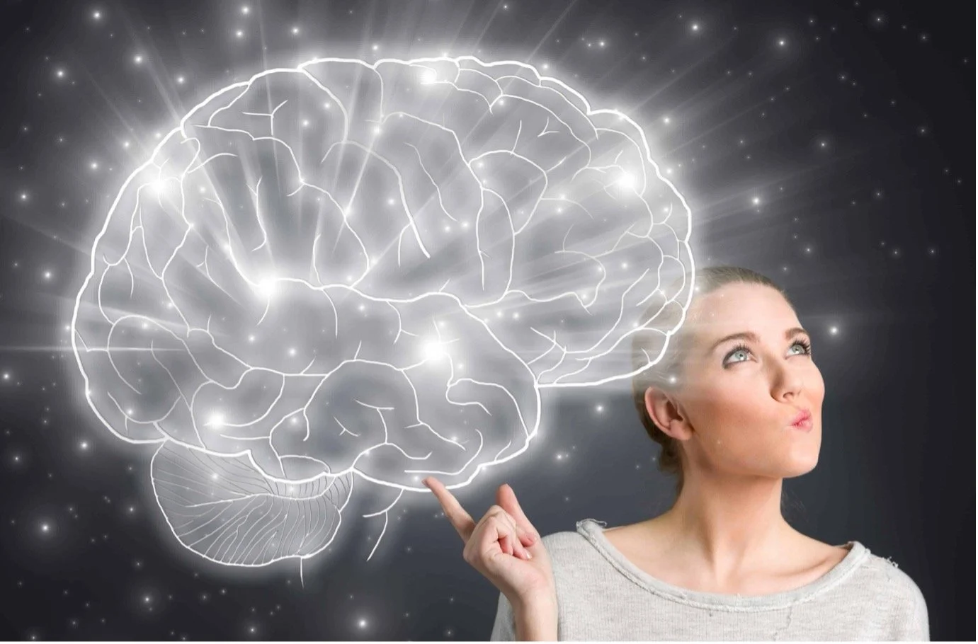 A woman with blonde hair and a gray shirt is touching a digital illustration of a bright, glowing human brain outlined with white lines, set against a dark background with sparks and light rays.
