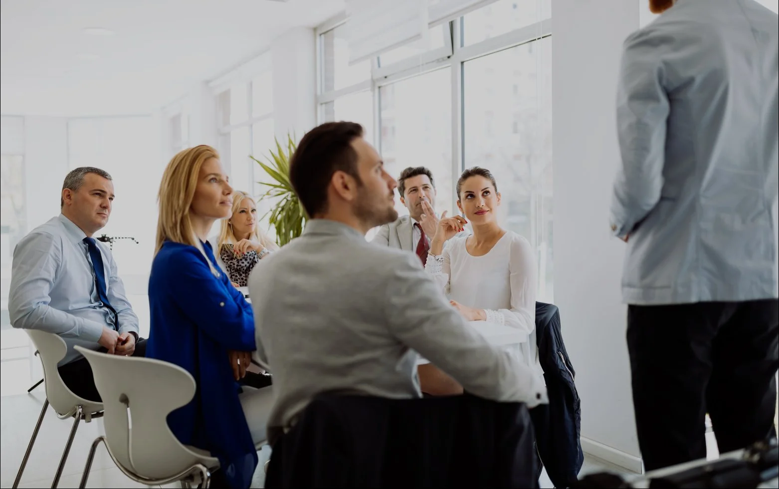 Group of professionals attending a seminar or meeting in a bright, modern office space with large windows.