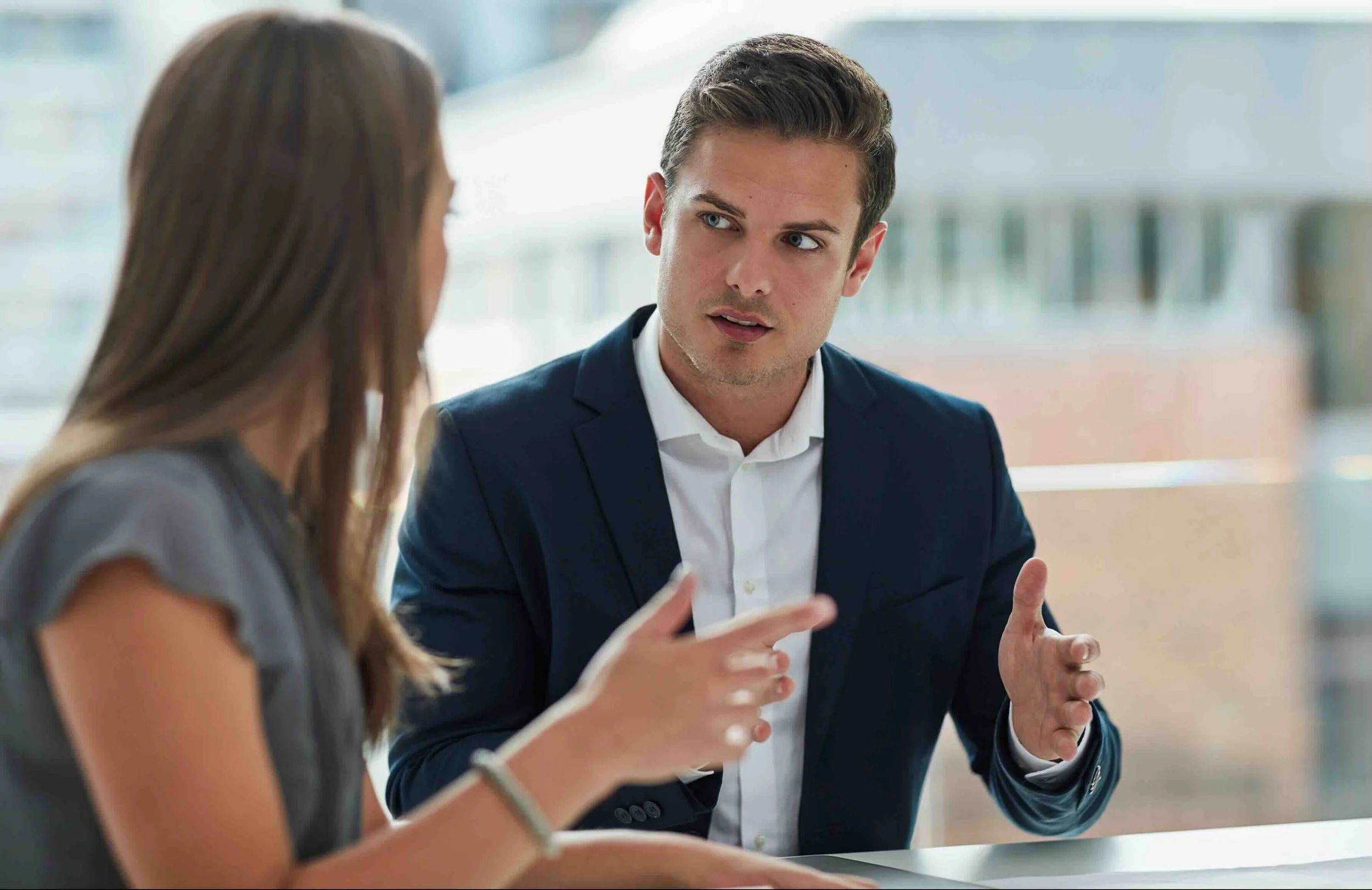 Man and woman engaged in a serious discussion at a meeting table in a modern office.
