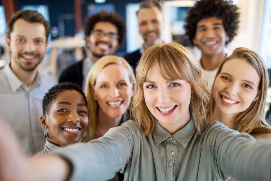 Group of smiling diverse young adults taking a selfie in a modern indoor setting.