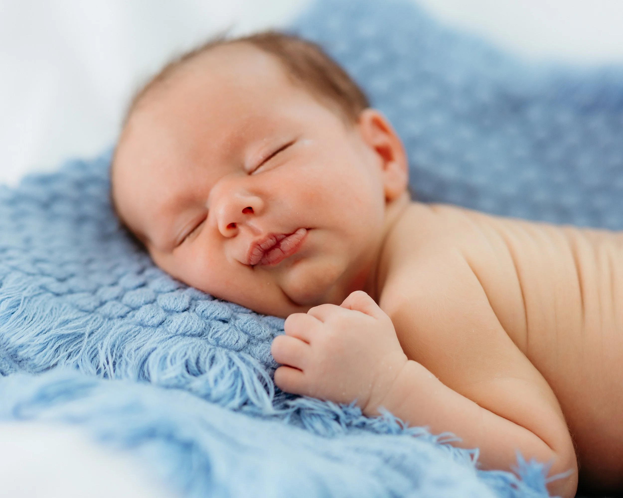 Close-up of an adult hand holding a baby's hand, both resting on a pastel-colored blanket.