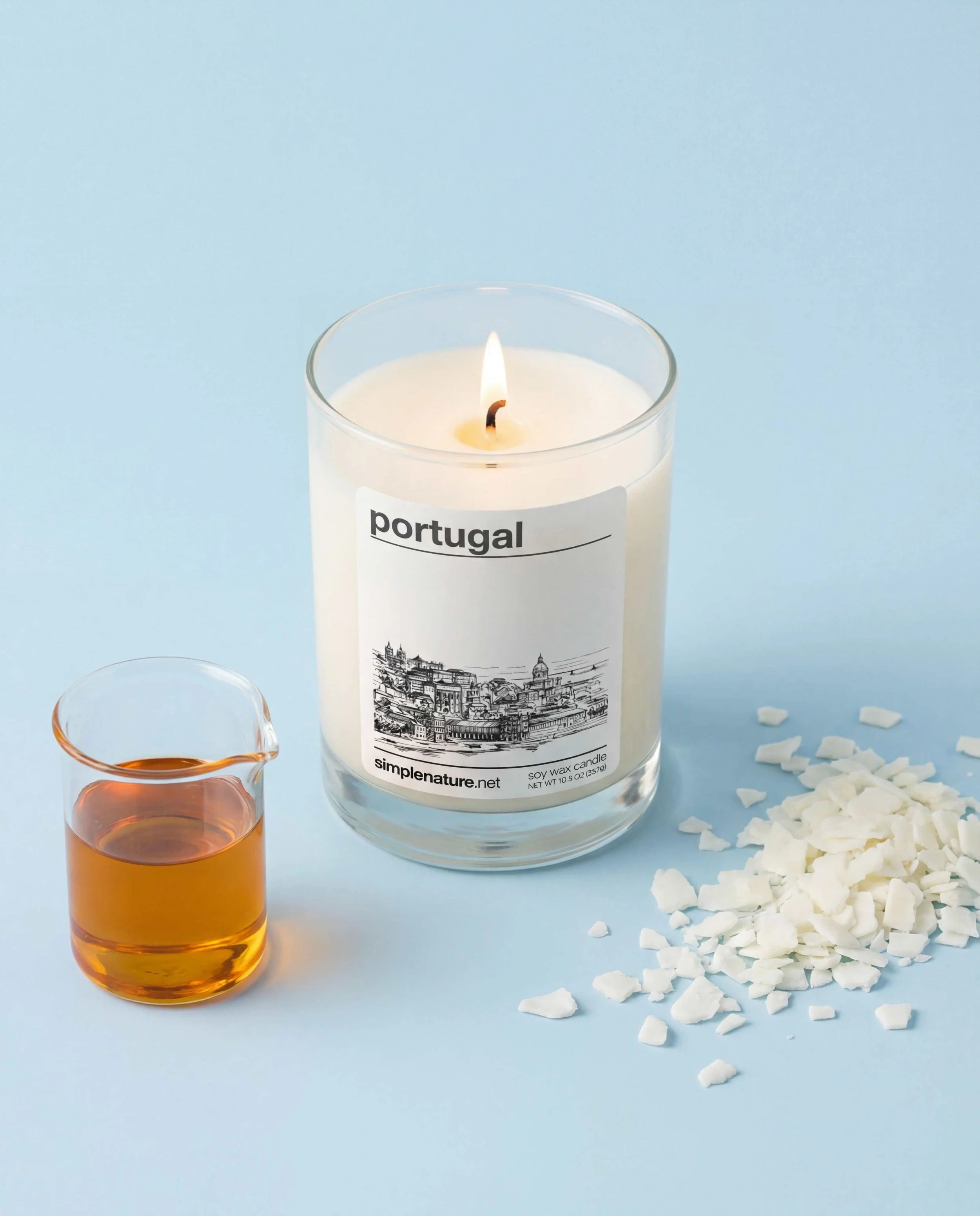 A lit candle surrounded by shot glasses filled with a yellow liquid, on a white surface with scattered white wax pieces.