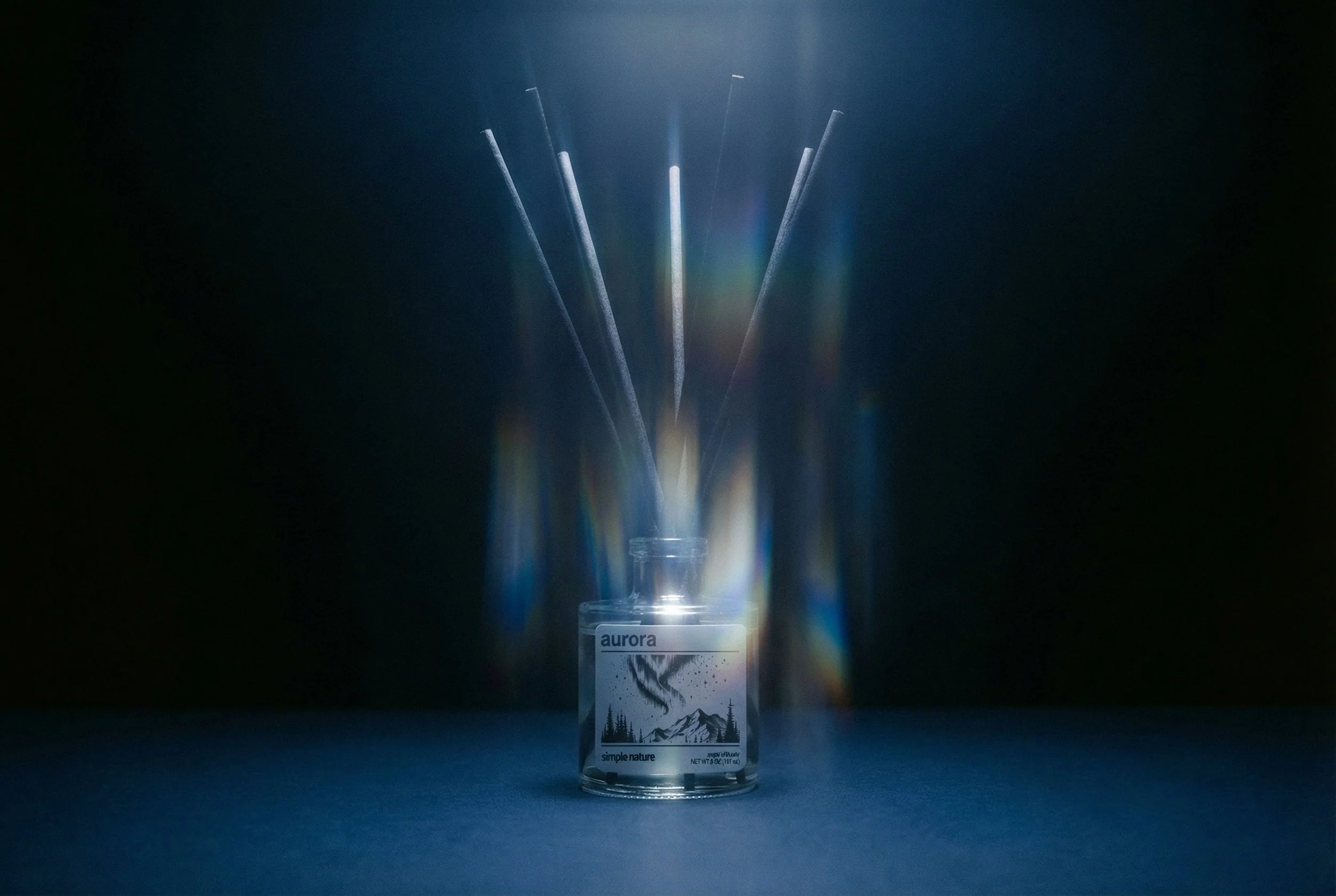 A glass jar labeled 'aurora' with a mountain and aurora borealis illustration, containing reed diffusers emitting colorful light reflections on a dark background.