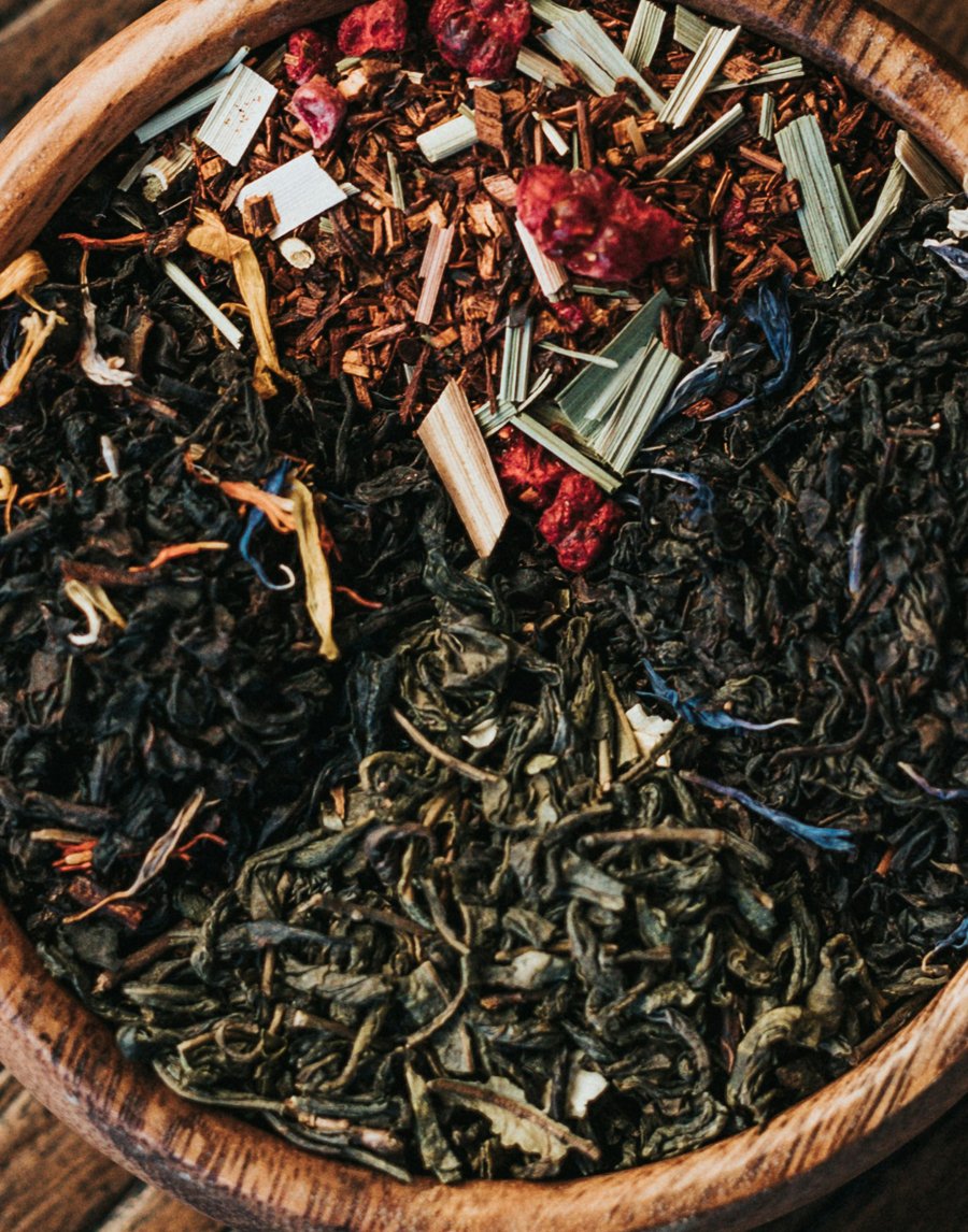 Close-up of dried loose leaf tea in a wooden bowl, with visible different types of tea leaves and herbal ingredients.