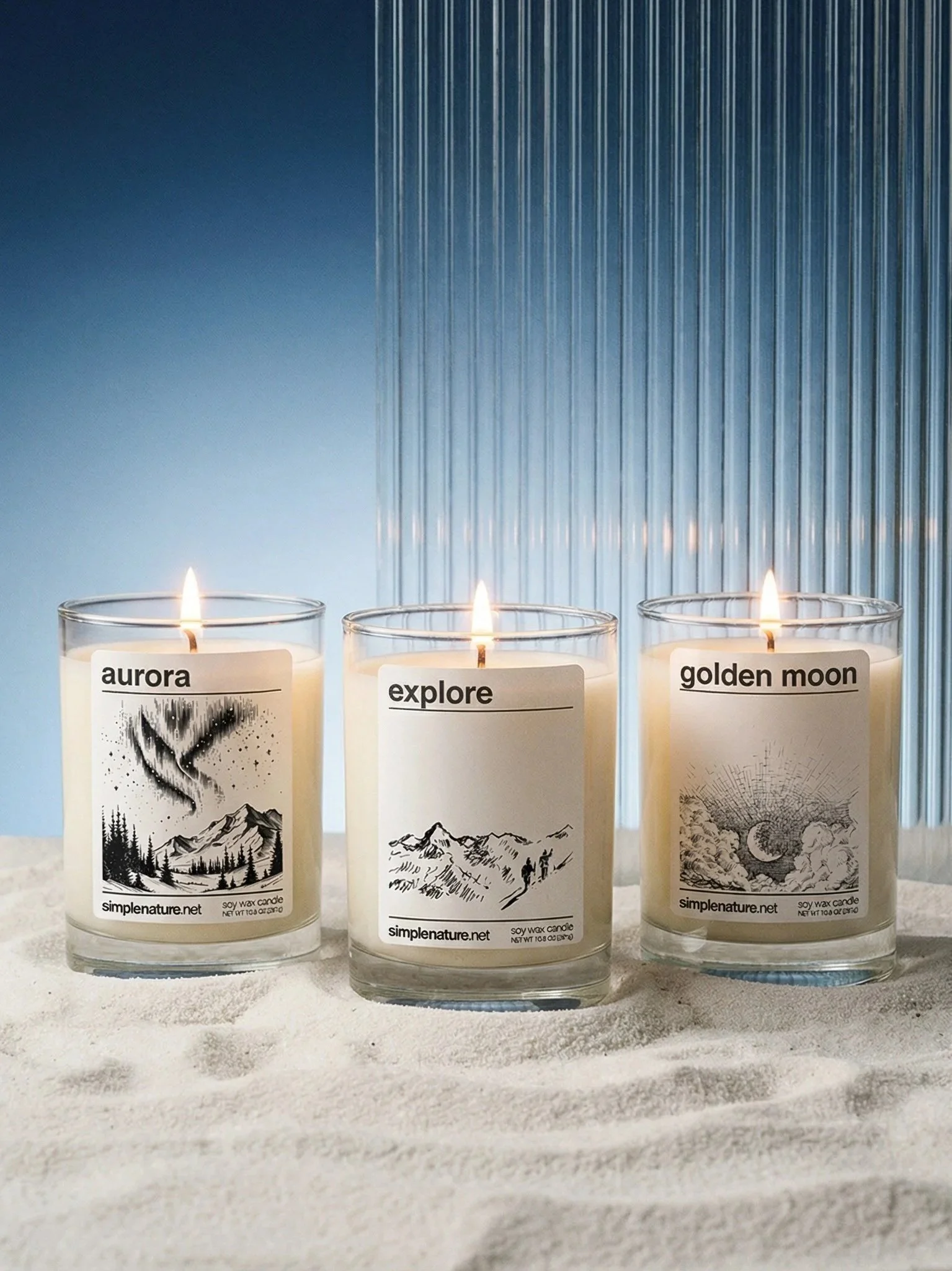 Three lit candles in glass containers with nature-themed labels reading 'aurora,' 'explore,' and 'golden moon'; they are on a textured white surface with a metallic blue corrugated background.