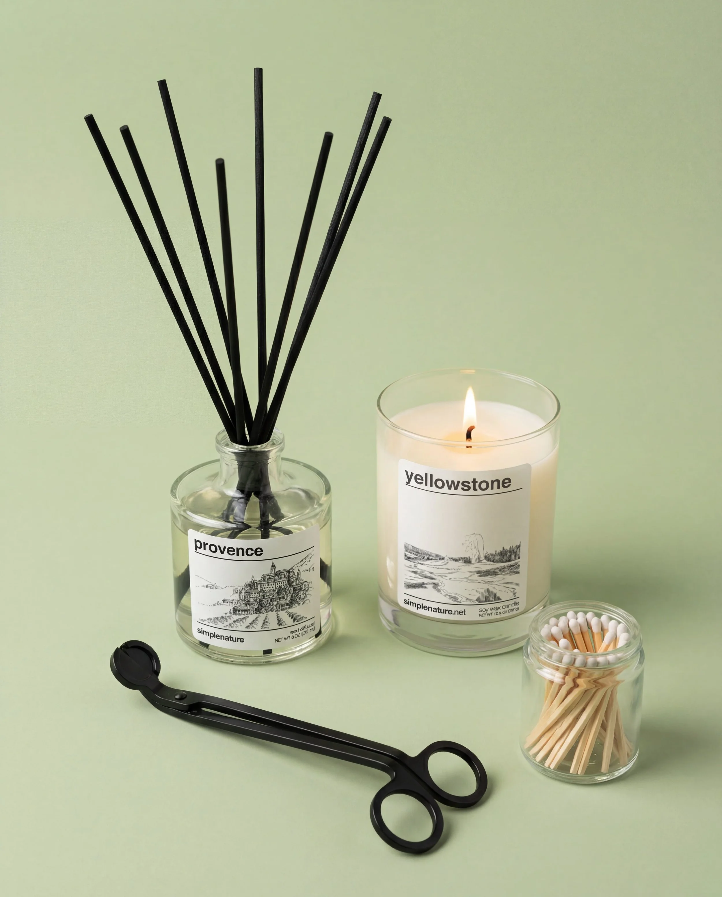 A hand is lighting a candle labeled 'Portugal' with a matchstick. The candle has a skyline illustration of Lisbon and a website link 'simplenature.net'. There is a box of matches and a black object on the white surface in the foreground.