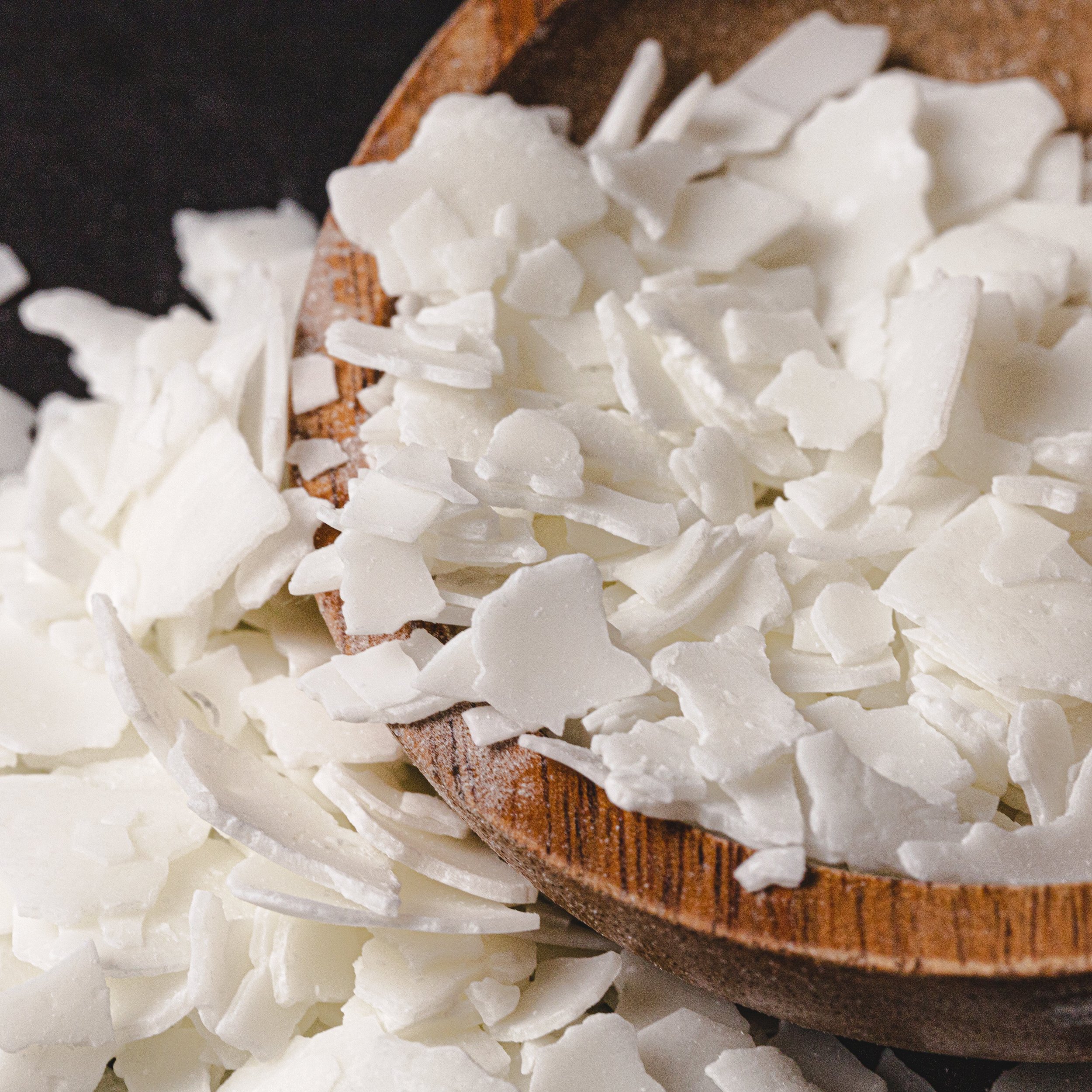 Close-up of white coconut flakes on a wooden spoon and scattered around it.