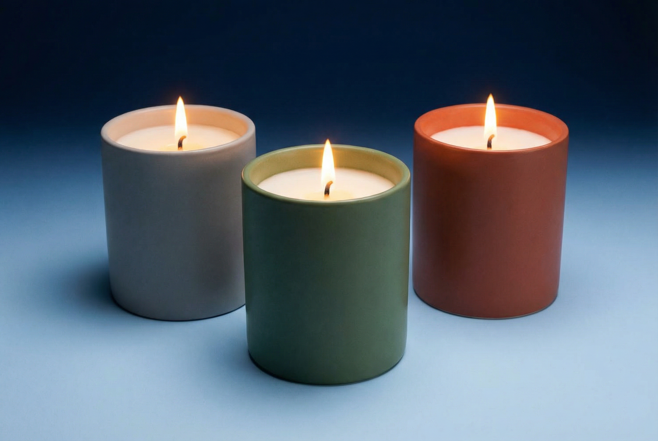 Three lit candles in pastel-colored holders (gray, green, and orange) on a gradient blue background.