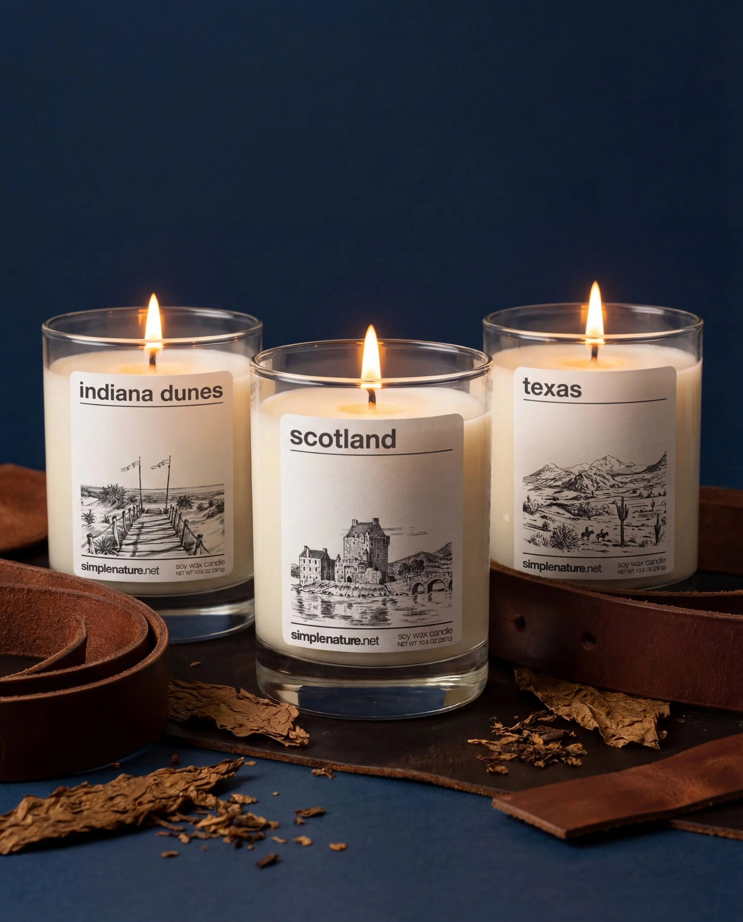 Two lit candles in glass holders placed on a wooden surface with moss and rocks. Each candle has a label with the words 'matterhorn' and 'fortitude,' along with line drawings of mountain scenes.