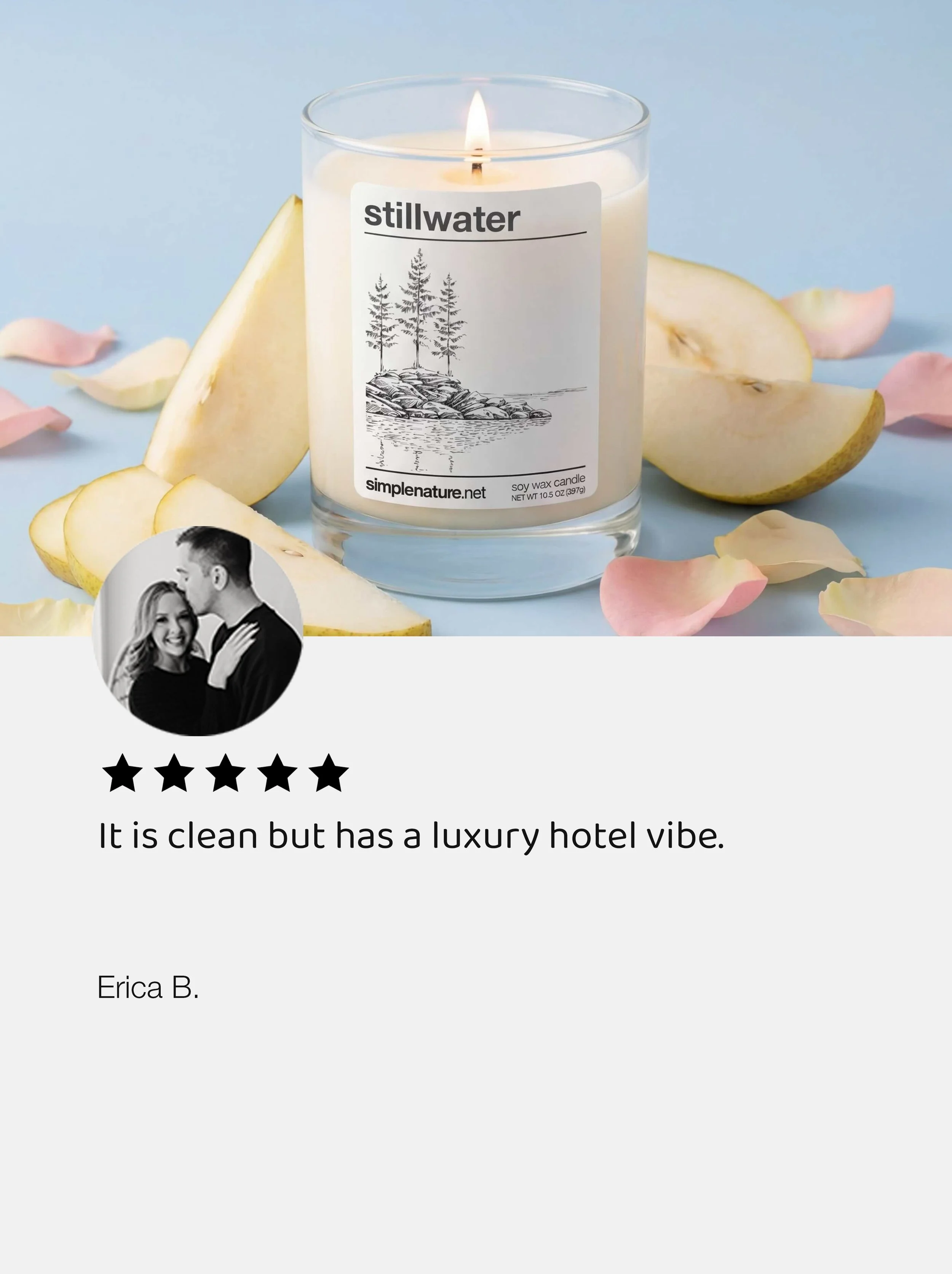 A white candle labeled 'stillwater' with a drawing of trees and rocks, surrounded by apple slices and rose petals on a light blue background.