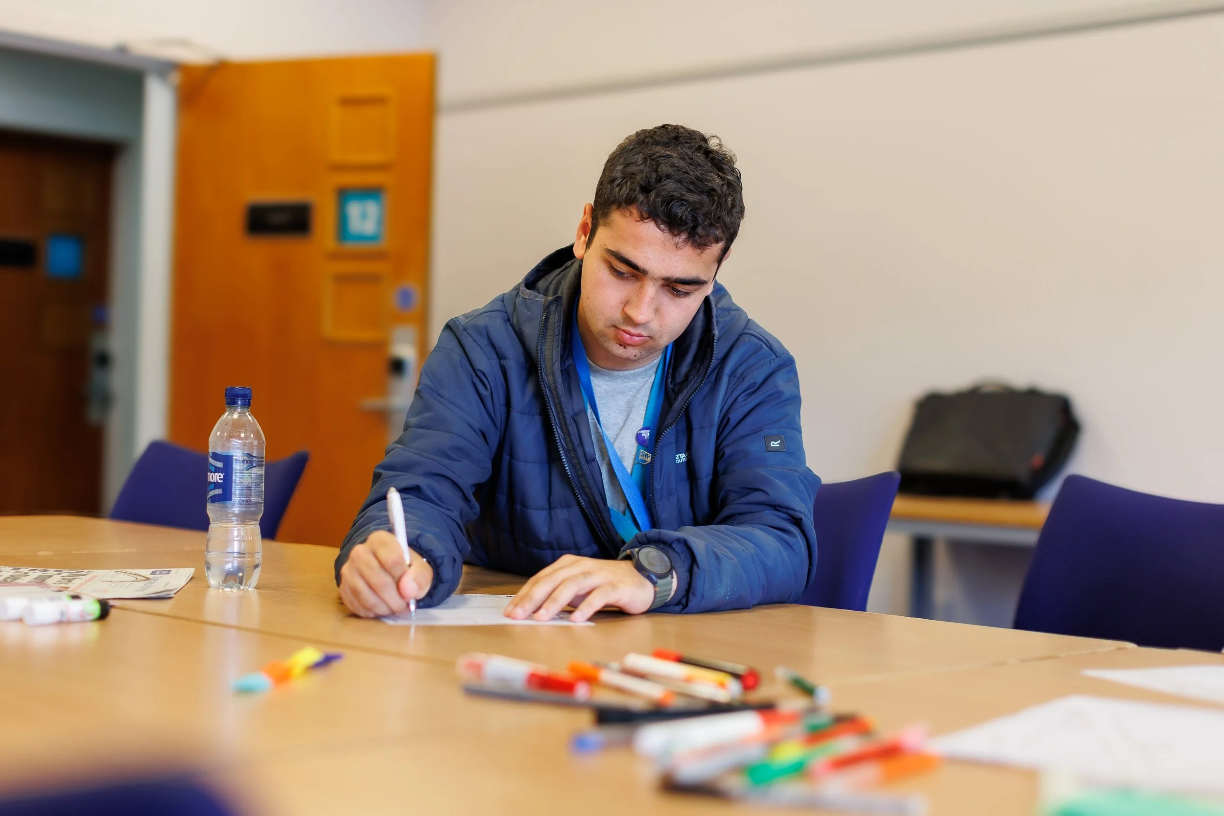 An MSYP wearing a blue jacket and writing on a piece on paper while sitting on a table