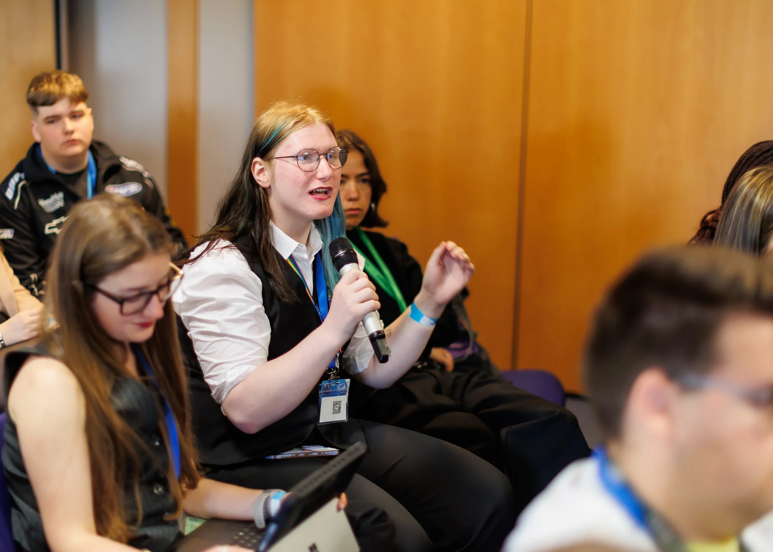 A Member of the Scottish Youth Parliament holding a microphone in a room with other members