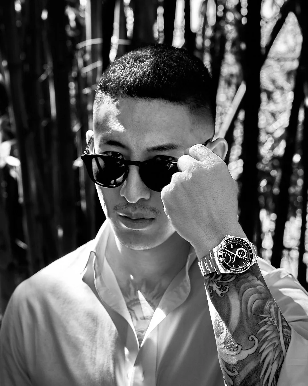 Asian tattooed male model wearing a black dial pulsometer men’s fine watch looking into camera while holding his sunglasses