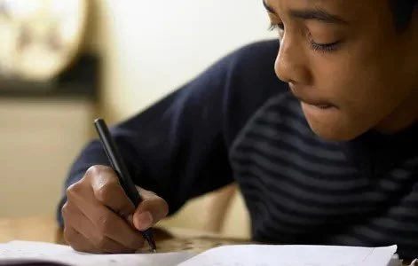Student writing notes with a pen at a desk