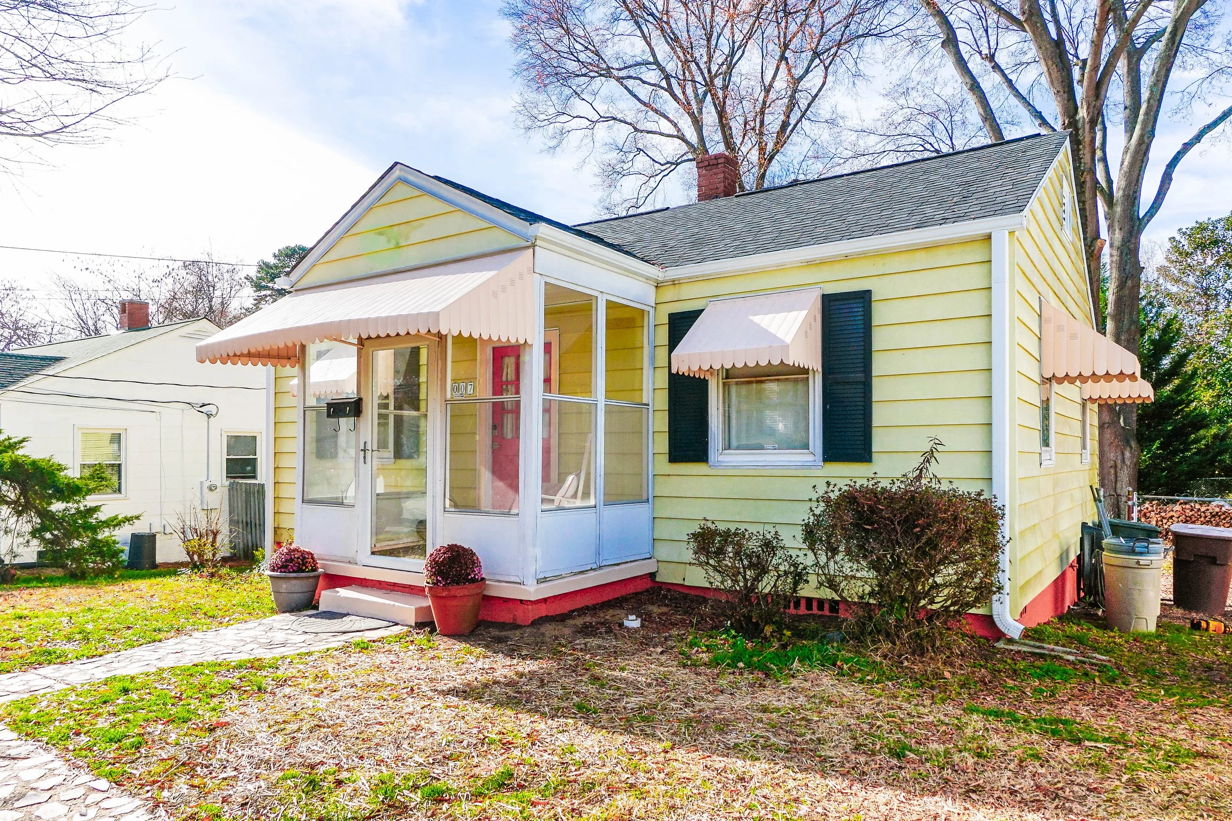 Living room with red and brown furniture, a ceiling fan, window blinds, and a patterned rug. Open kitchen with red cabinets and a bar with two chairs.