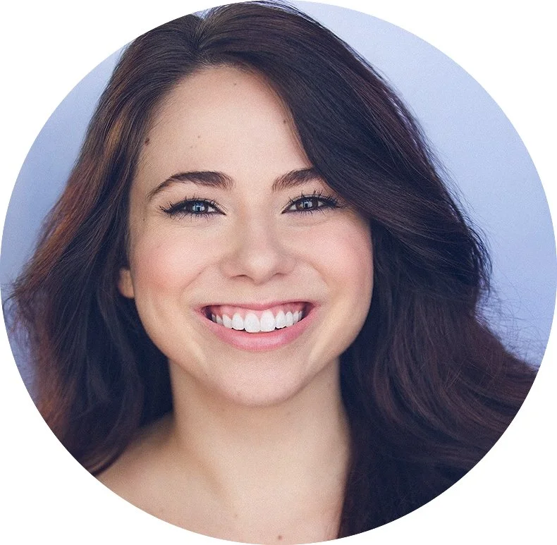 Close-up of a woman with long, dark hair, smiling and showing her teeth, against a neutral background.
