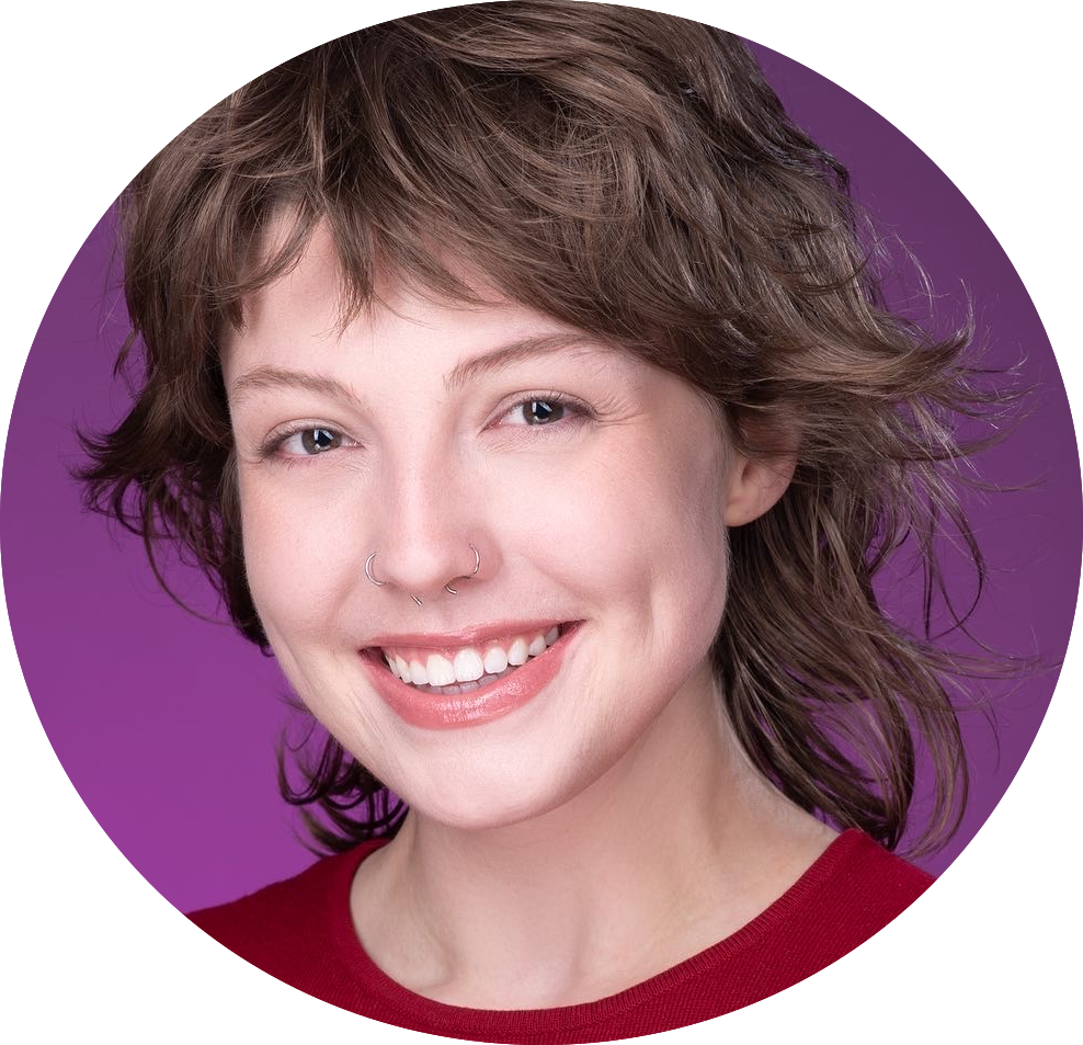 A woman with short, wavy brown hair, blue eyes, and a nose piercing, smiling against a purple background, wearing a red top.