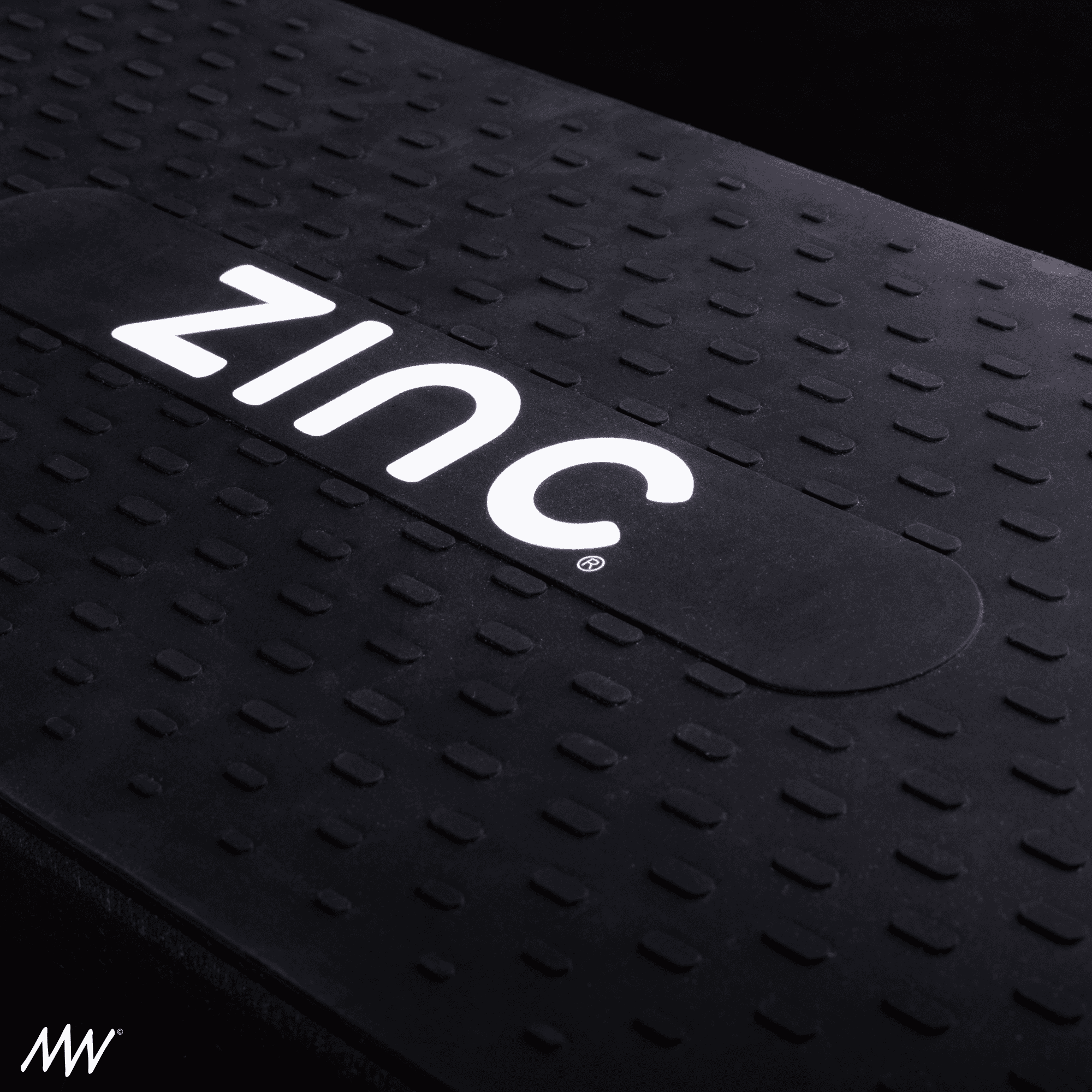Close-up of a black skateboard with white illuminated ZINC logo on the deck, featuring textured grip surface.