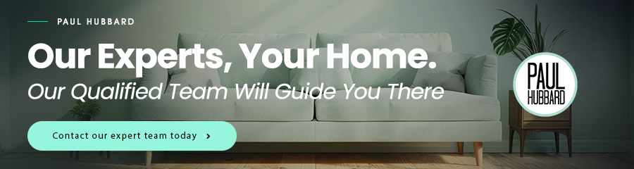 Living room with a white sofa, green plants, and a wall with promotional text about a home expert team and a contact button.