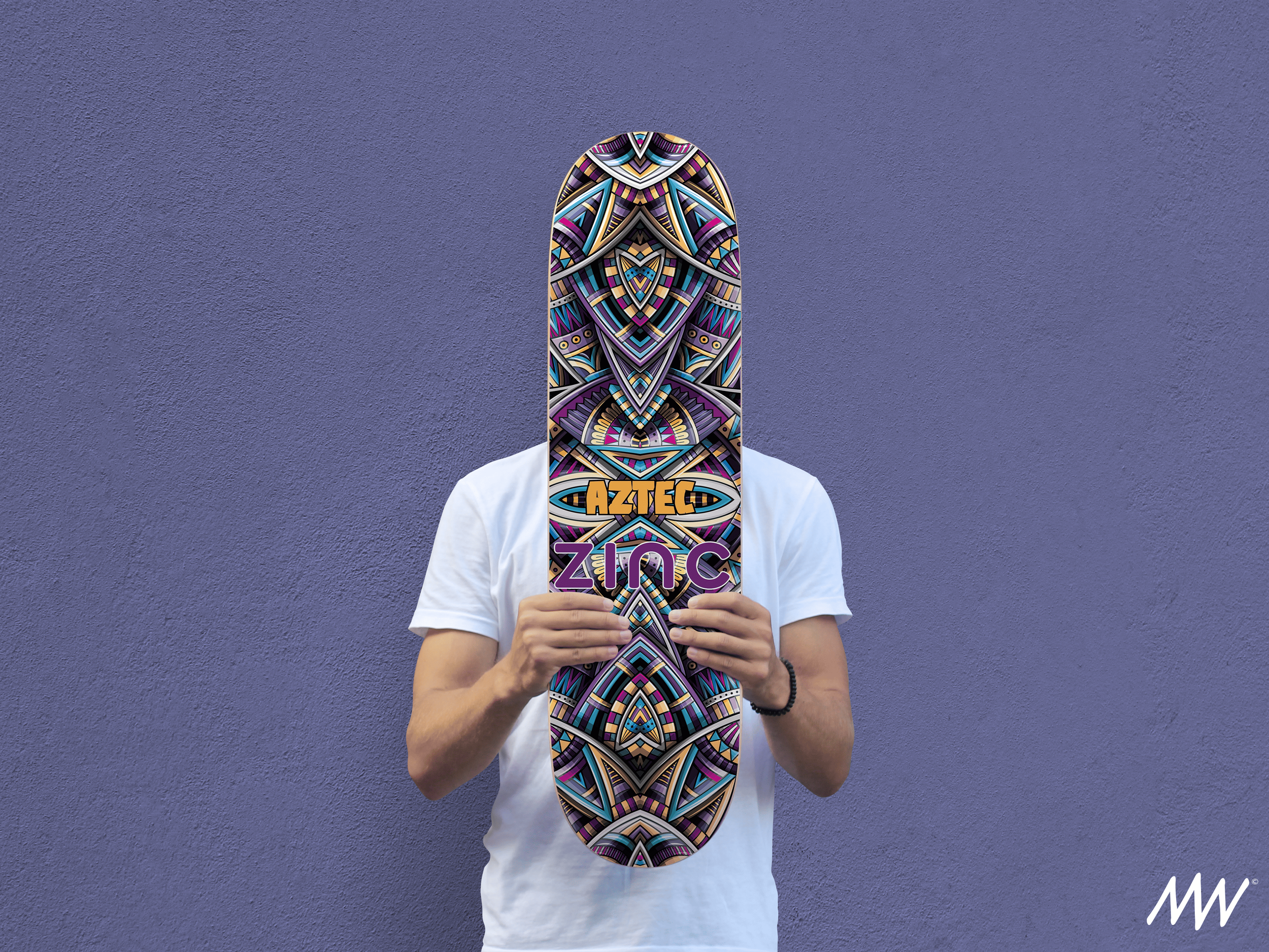 Person holding a skateboard with a colorful, intricate tribal design, obscuring their face, standing against a purple wall