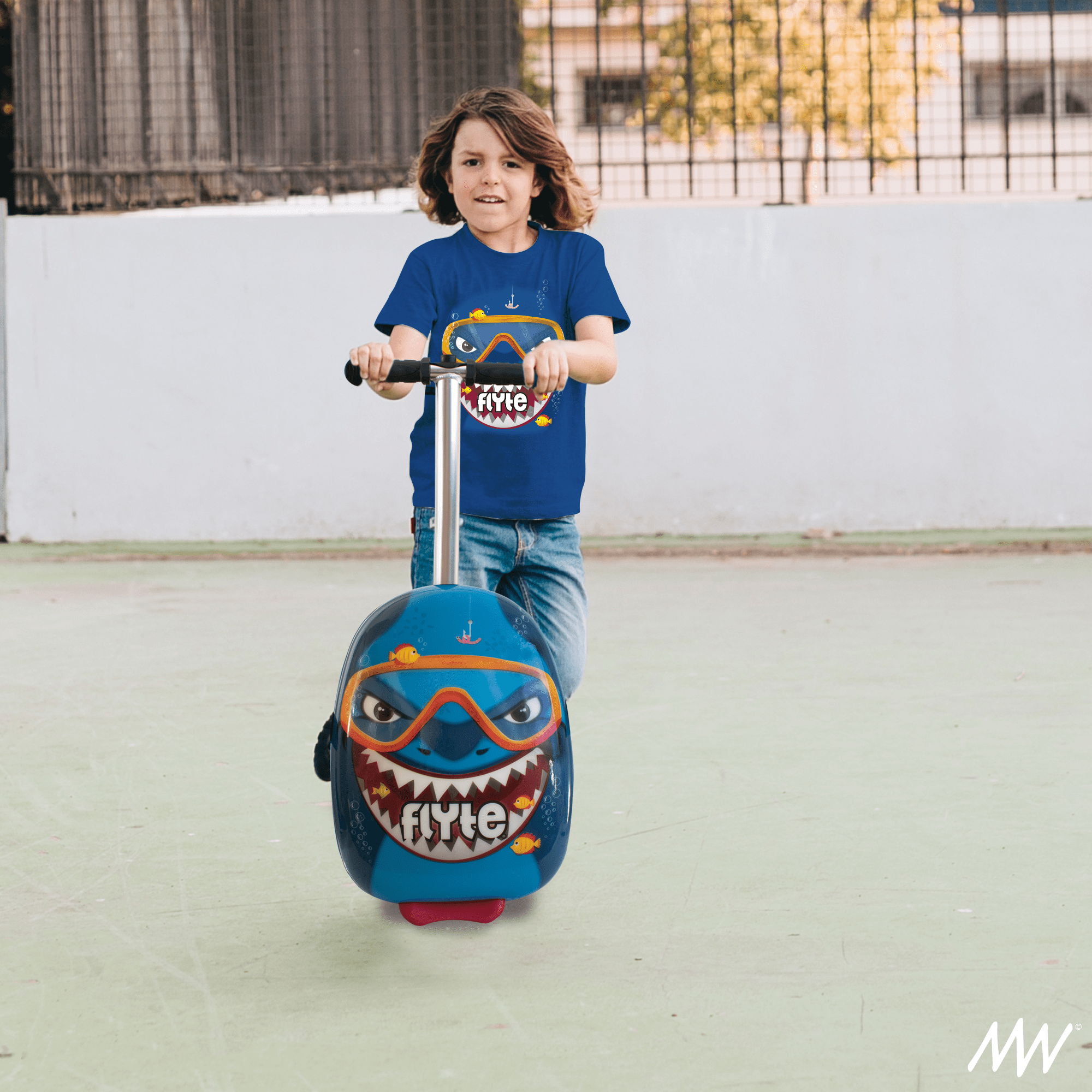 A young boy riding a blue scooter with a cartoon shark face design and the word 'Flyte' on the front, outdoors on a concrete surface.