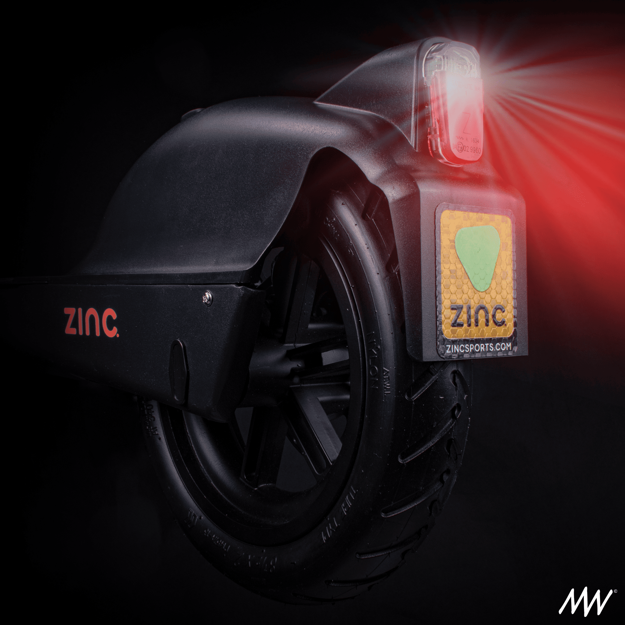 Close-up of a self-balancing electric unicycle with a black body, branded 'Zinc,' showing a rear light emitting red rays, a tire, and a reflective sticker with the Zinc logo.