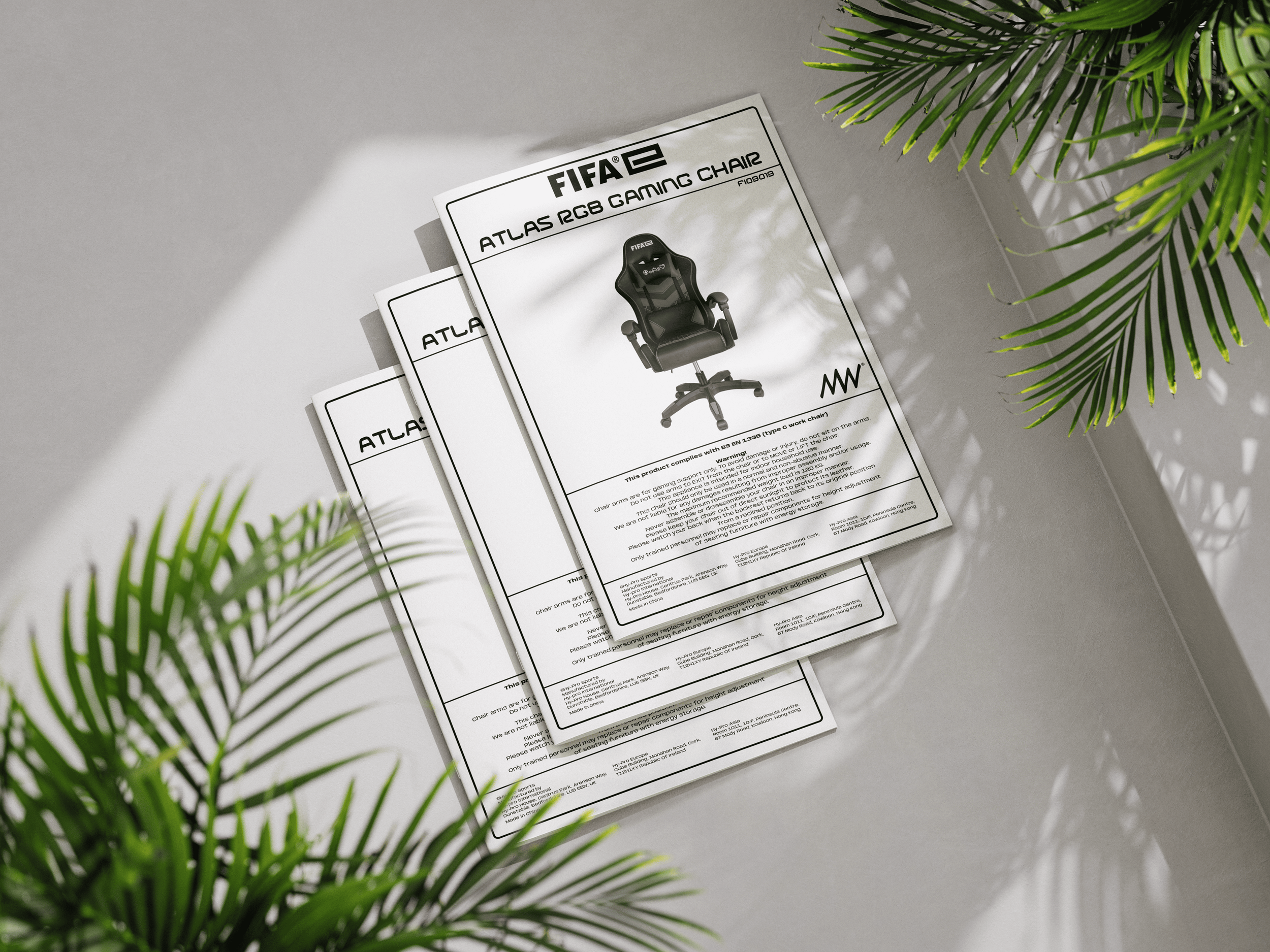 Instruction manuals for an Atlas RGB gaming chair, with a picture of the chair on the front page, placed on a light-colored surface with green plant leaves in the foreground and background.