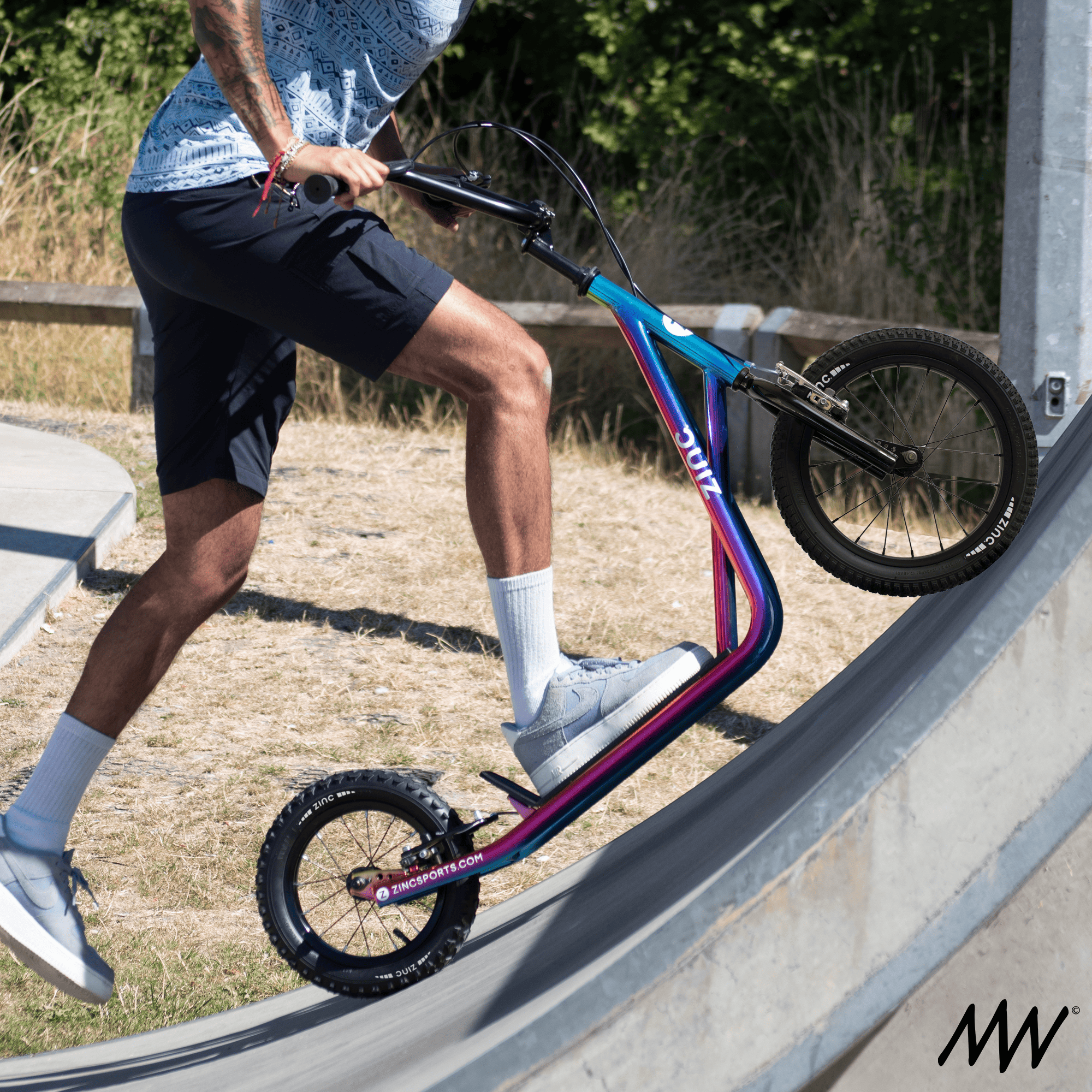 Person riding a colorful BMX bike up a ramp outdoors with trees and grass in the background.