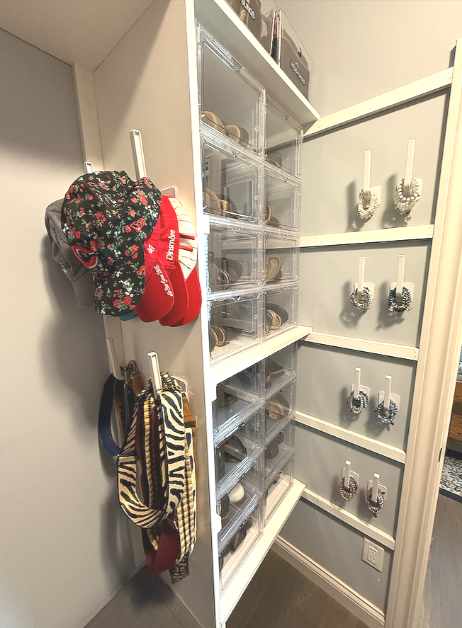 Organized closet corner with transparent shoe storage drawers, hanging hats, and scarves.