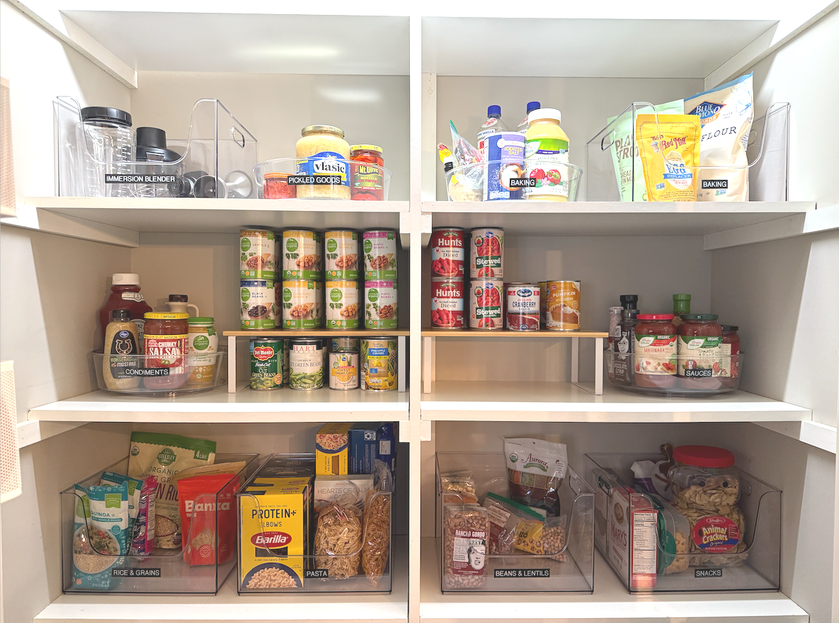 Open pantry with shelves holding canned goods, condiments, pasta, grains, snacks, and bottled beverages.