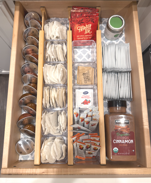 Kitchen drawer with coffee pods, napkins, tea packets, crushed red pepper, cinnamon ground spice, and utensils.