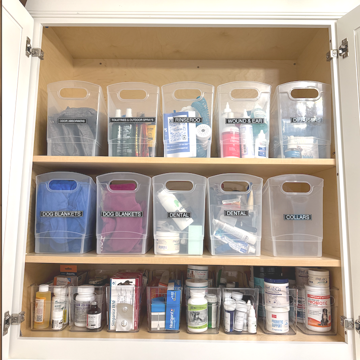 Cabinet with three shelves containing labeled plastic bins and bottles of medications and health products.