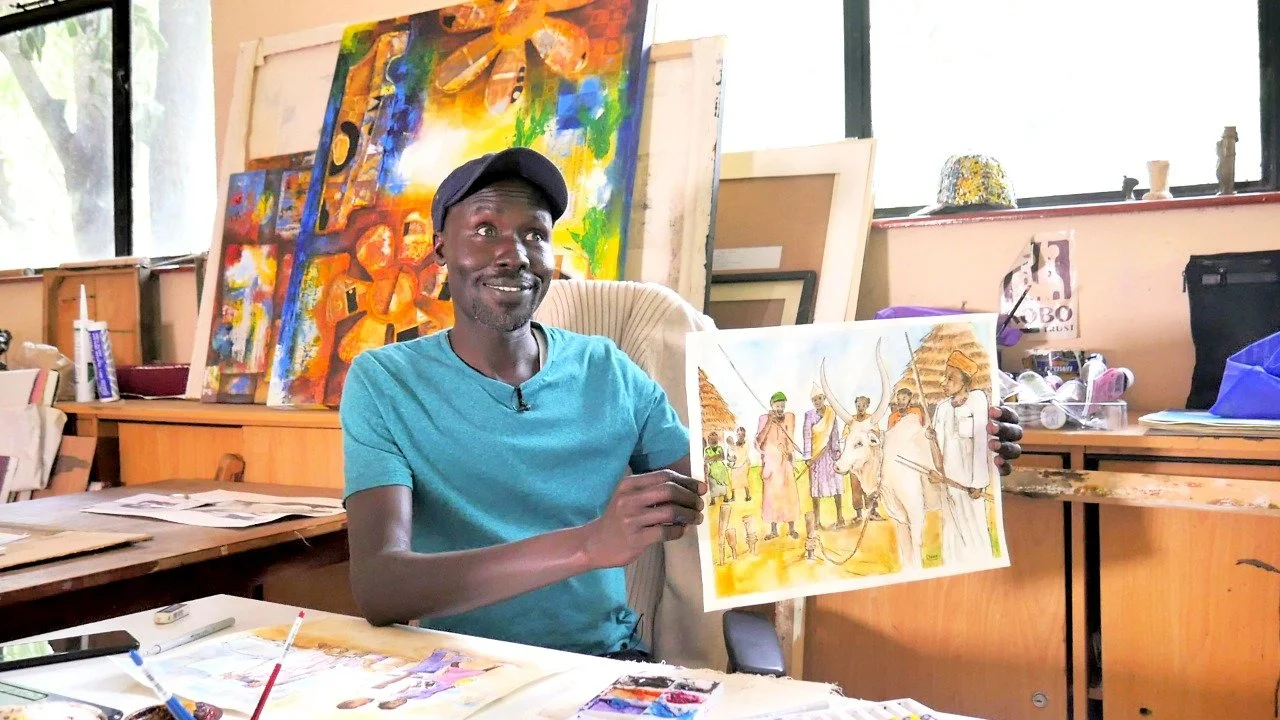 An artist in his colorful studio holds up a vibrant illustration he created.