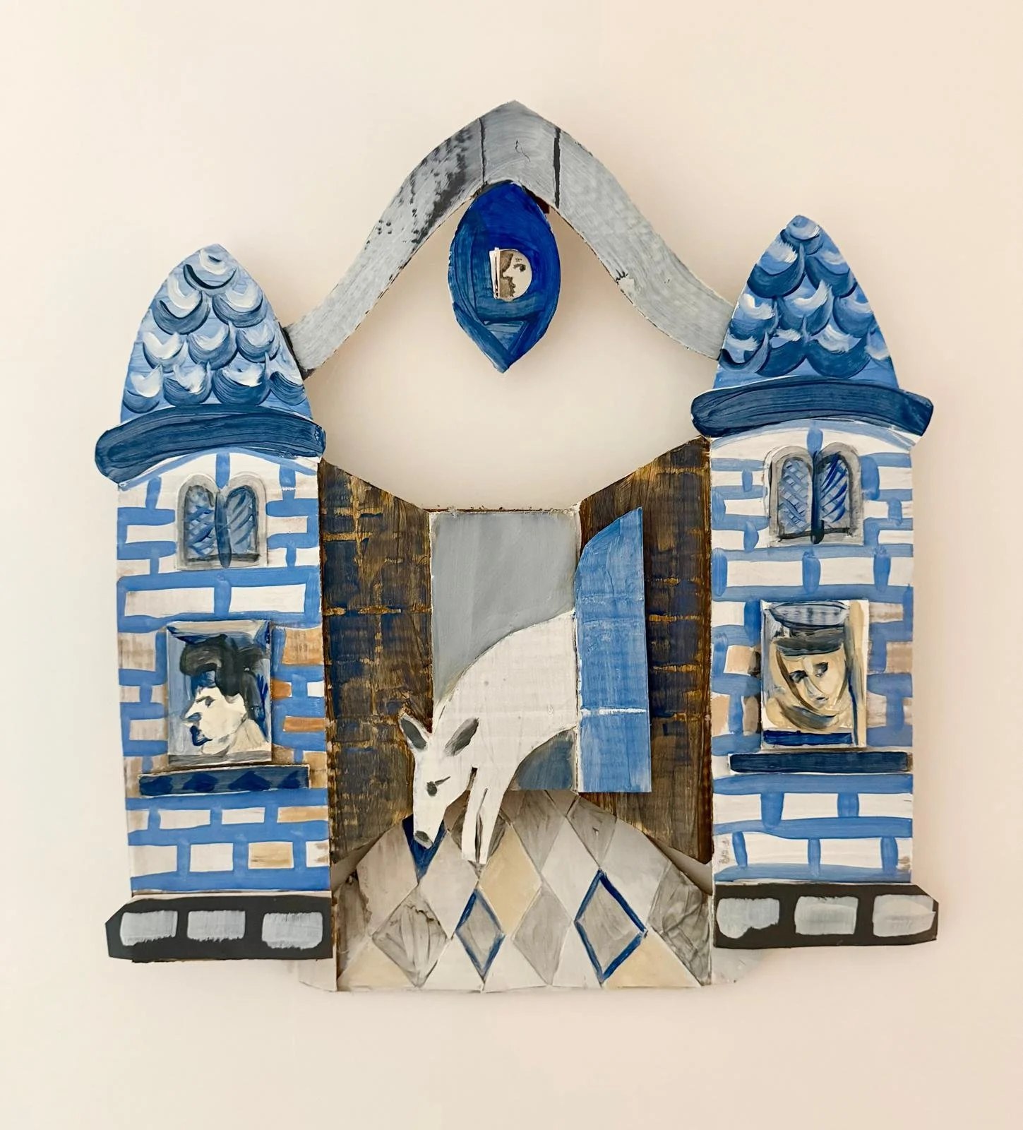Painted wooden cardboard cutout of a castle with a white wolf howling in front, blue conical towers, and portraits of a man and a woman in windows, on a beige background.