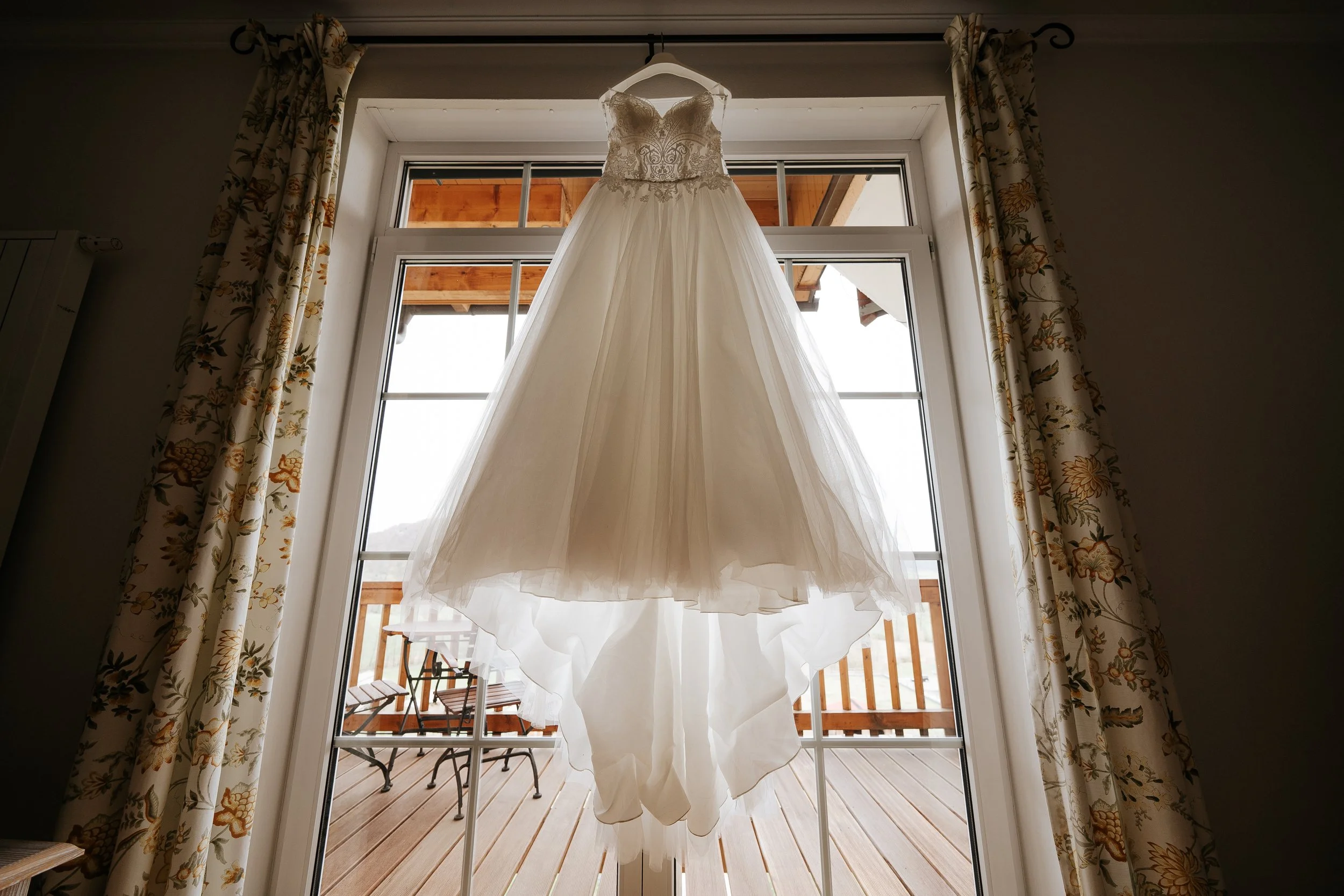 Weiße Hochzeitskleid hängt vor einem Fenster auf einer Terrasse.