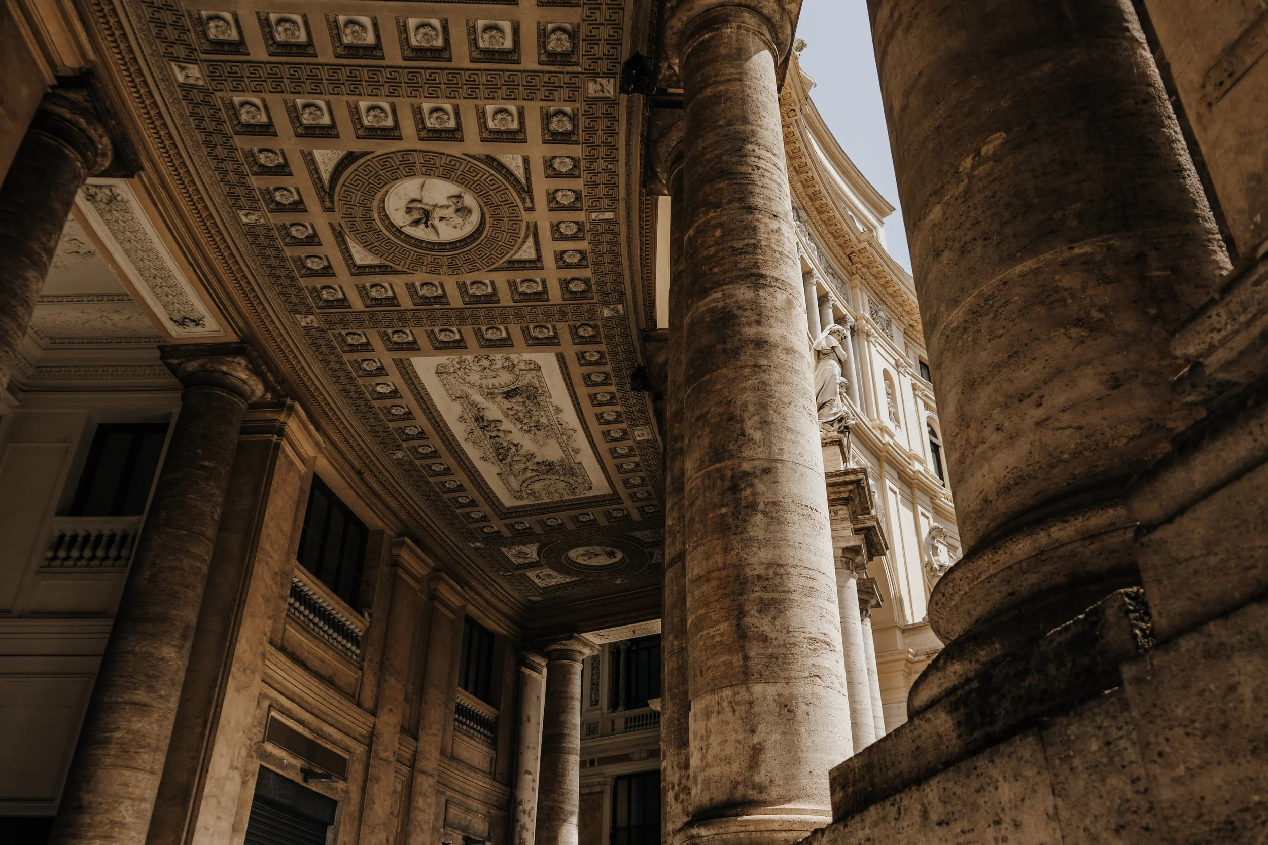 Blick nach oben auf eine historische Gebäudefassade mit großen Säulen und detaillierten Deckenverzierungen