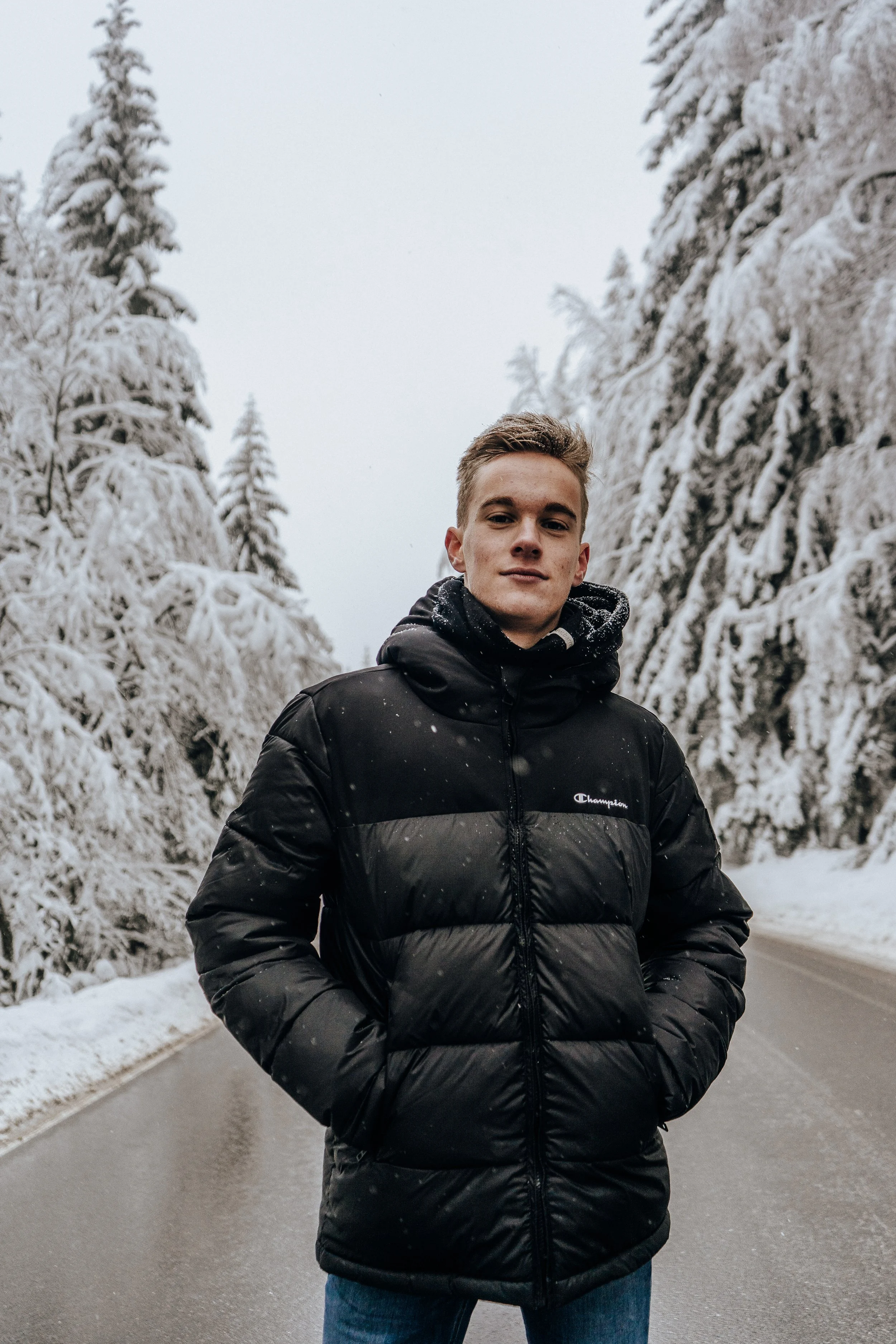 Mädchen steht auf einer schneebedeckten Straße in einem verschneiten Wald bei winterlichem Wetter.