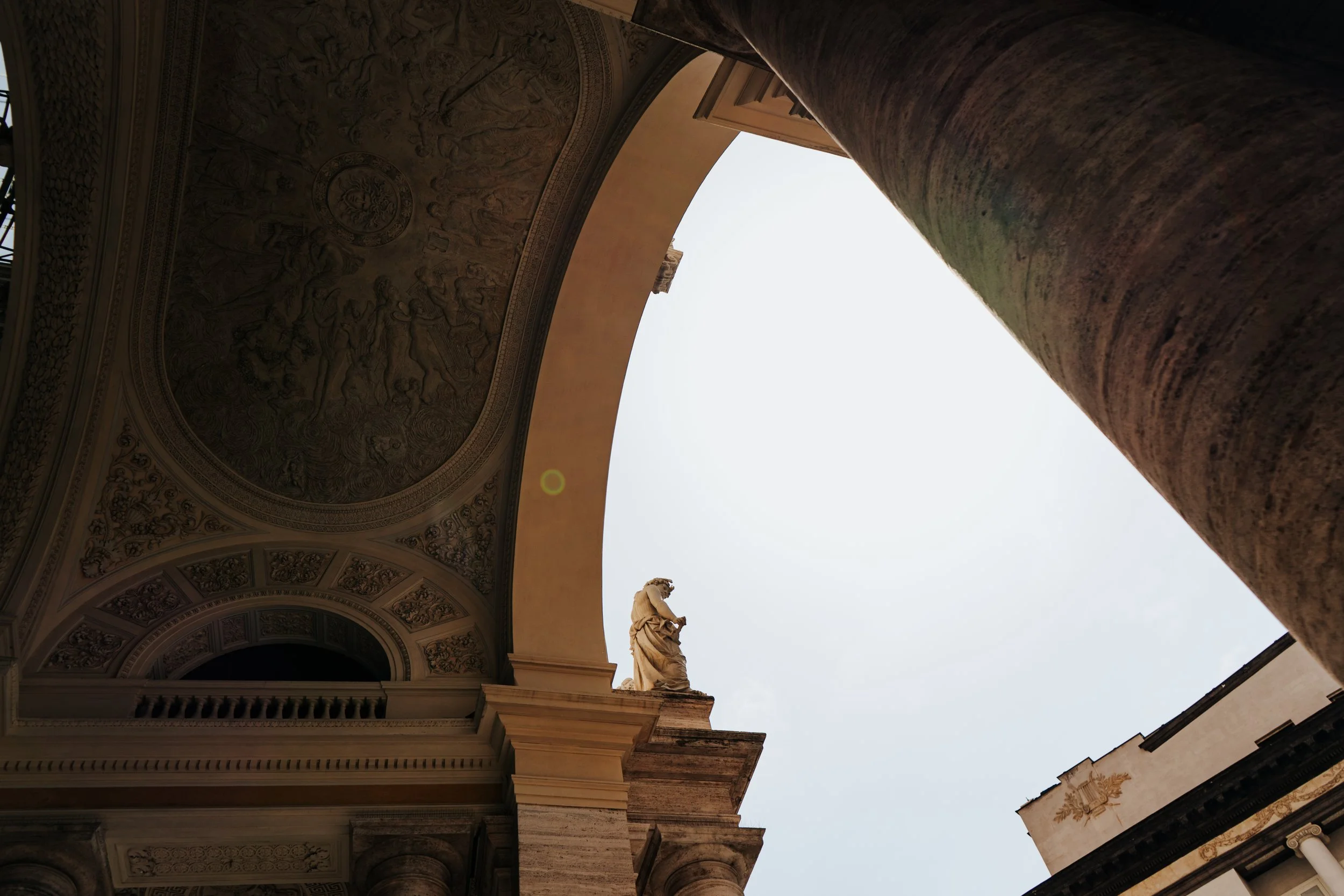 Aufnahme eines Gebäudebogens mit Verzierungen und einer Statue, Blick nach oben zur hellen, wolkenfreien Himmelsszene.