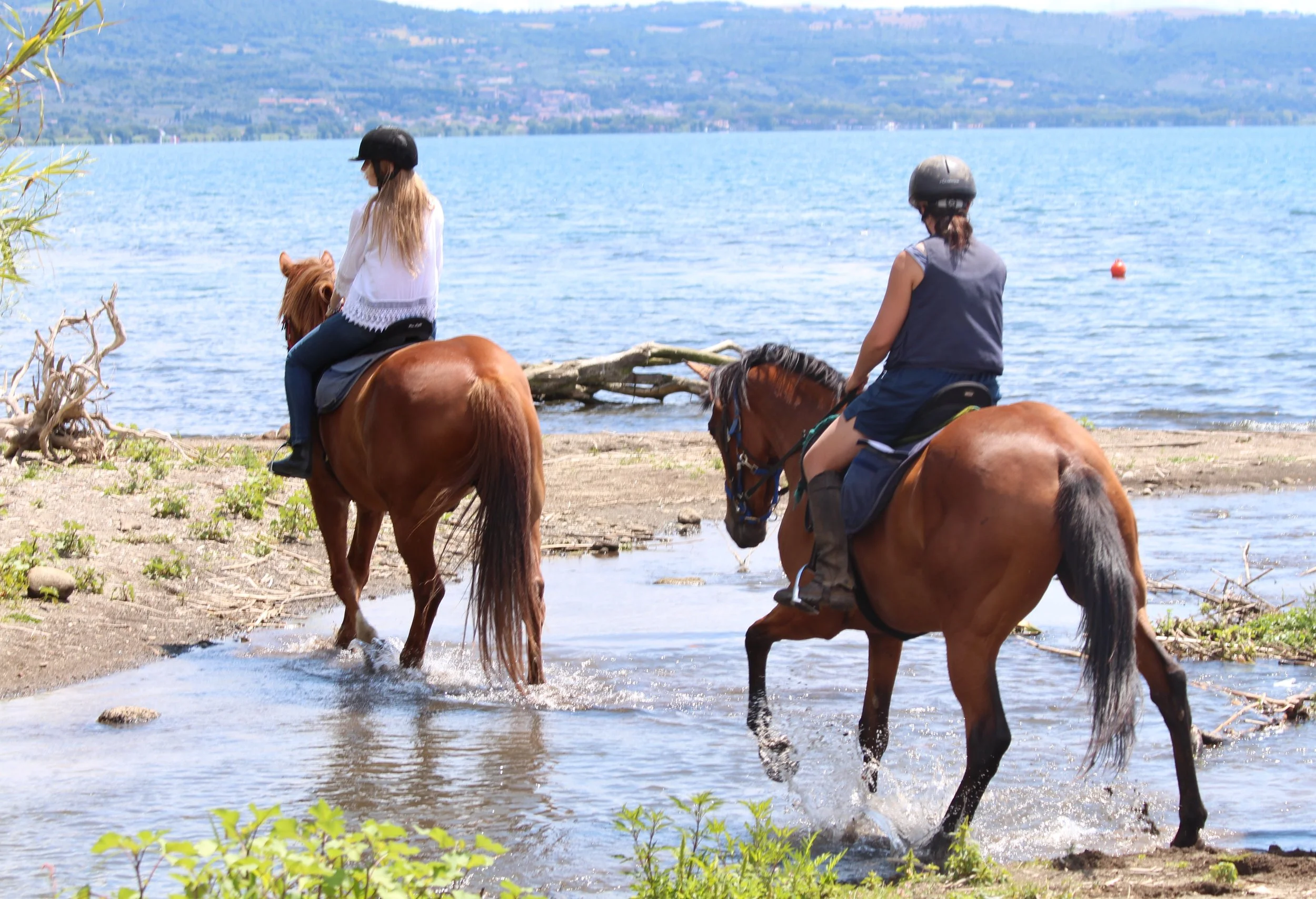 Two riders crossing a stream next to a lake in Lazio, Italy. 