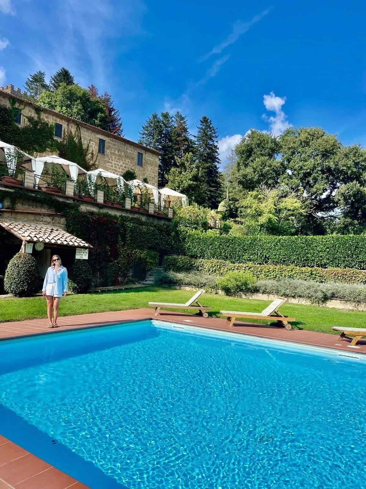 A swimming pool in the foreground with an italian farmhouse in the background.