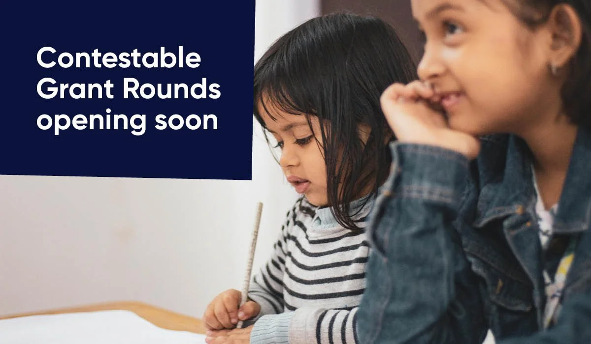 one girl smiling with her hands holding her jaw, and another girl writing. In the left corner is the words "Contestable Grant Rounds Opening Soon"