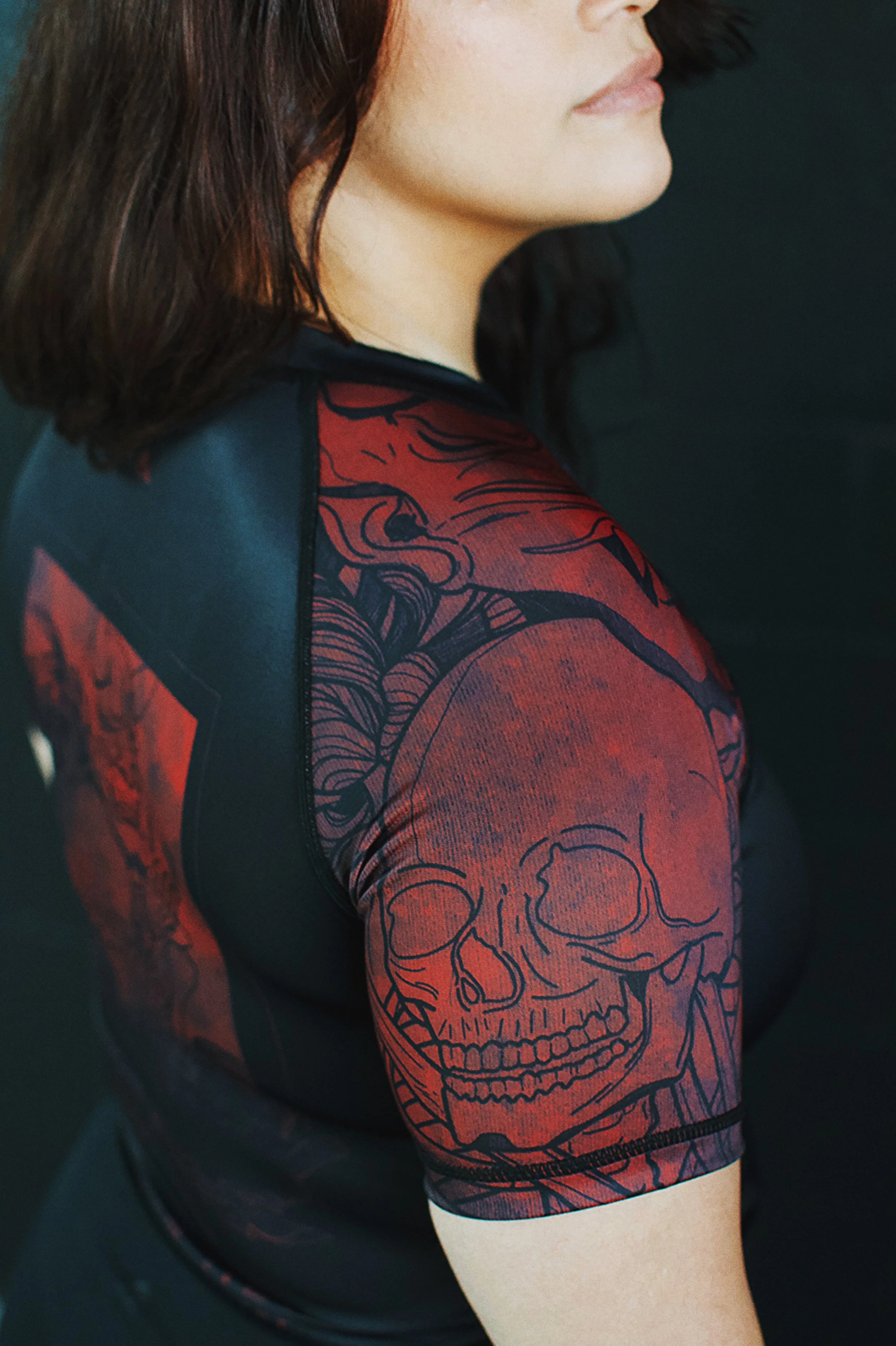 Close-up of a woman with shoulder-length brown hair wearing a black and red shirt with a skull and floral design on the sleeve.
