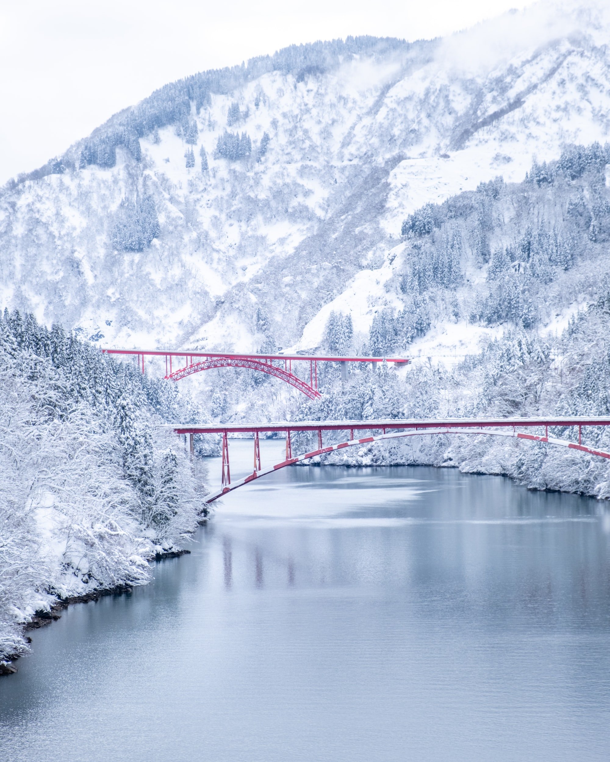 Snow-covered mountains with a river and red bridges.