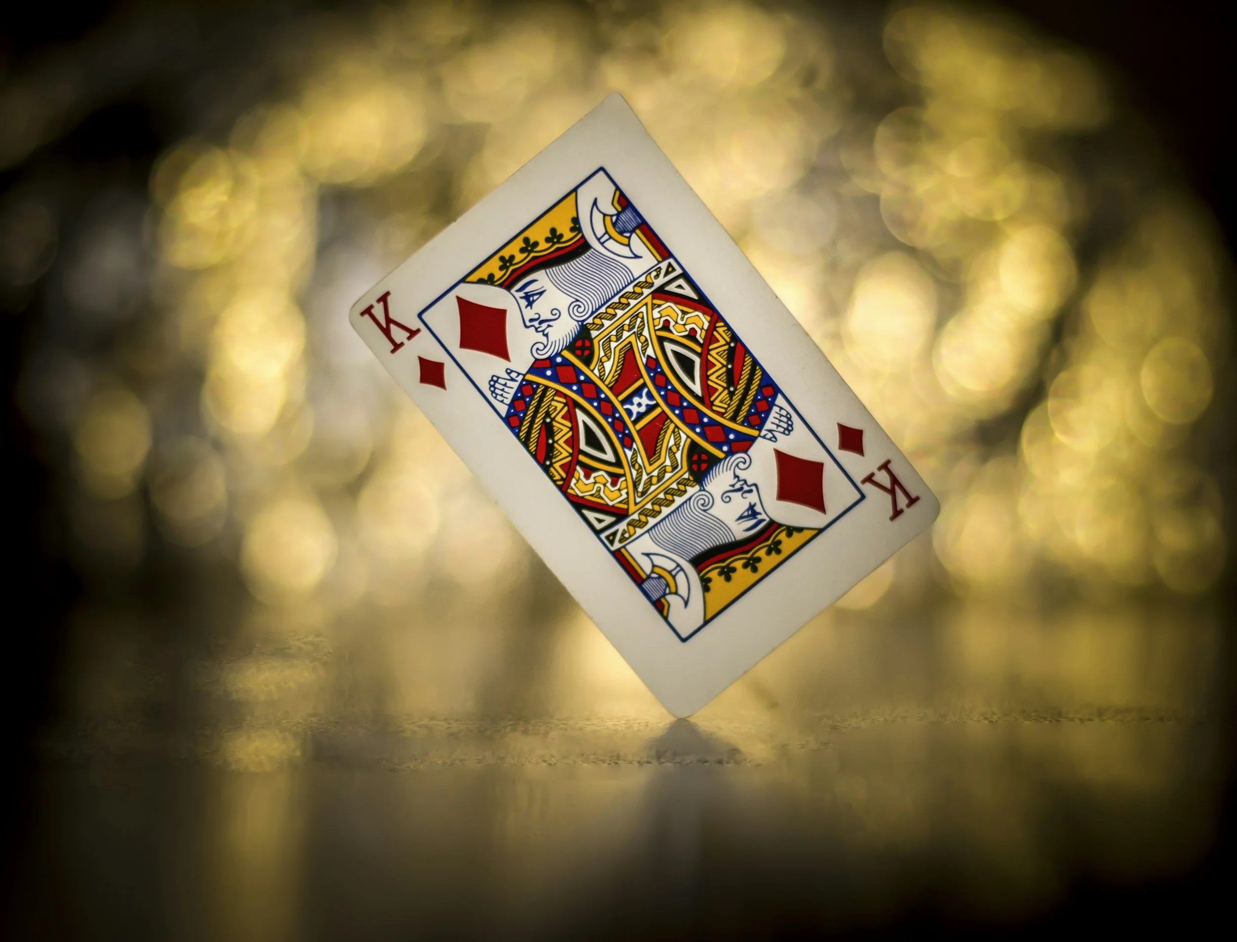 A playing card, the king of diamonds, is shown in close-up with a blurred background of golden bokeh lights.