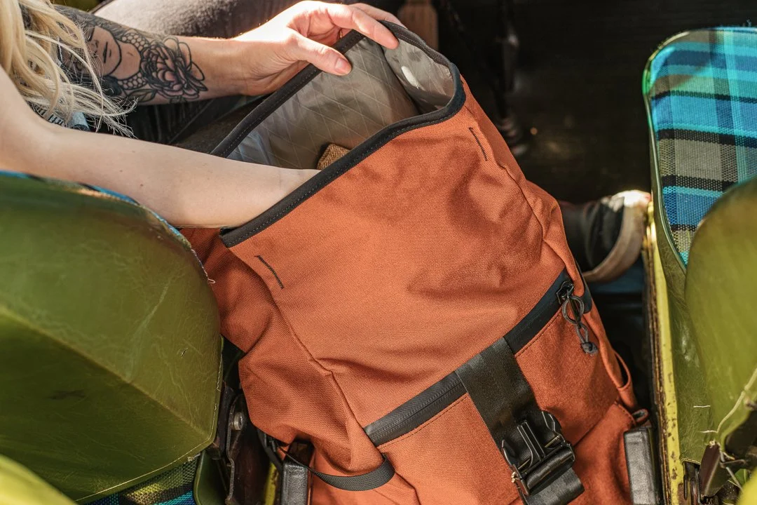 Person with a tattoo on their arm placing belongings into bike panniers, with an orange backpack inside the pannier.